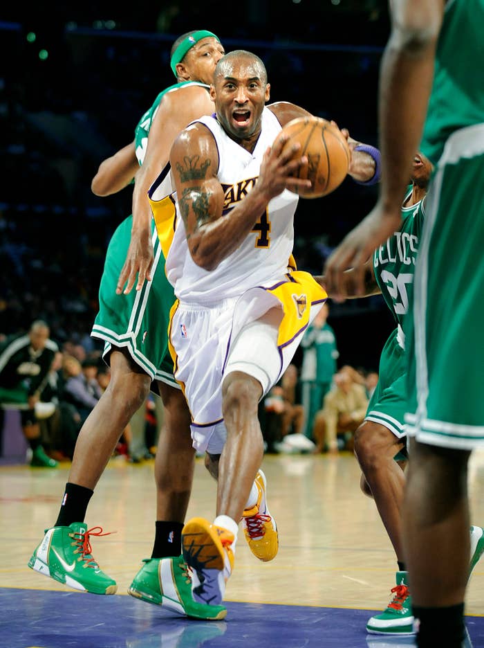 Kobe Bryant in white uniform drives to the basket, surrounded by opponents in green uniforms during a game