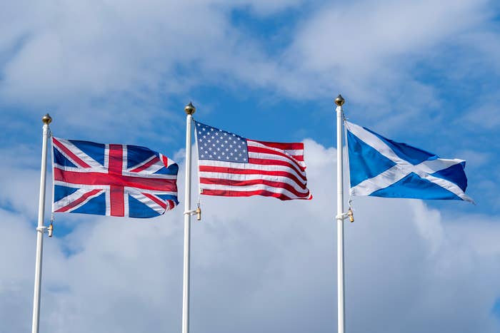  United Kingdom, United States, and Scotland flags waving against a cloudy sky