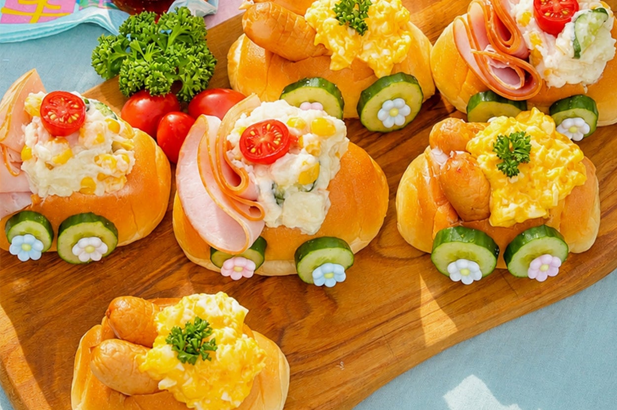 小さなパンに卵サラダ、キュウリ、ハム、トマトが載った華やかなオープンサンドイッチが木のプレートに載っている。