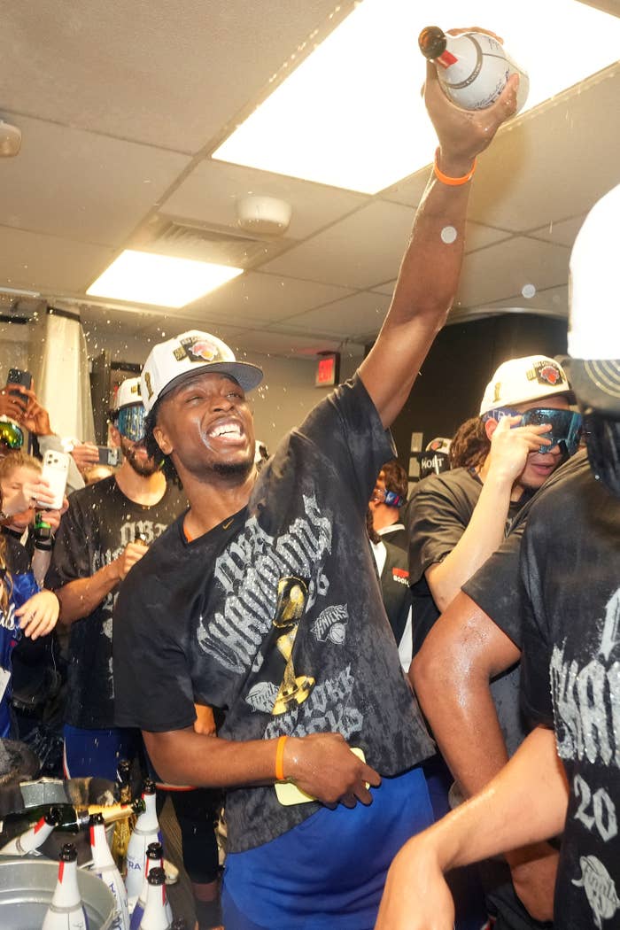 Athlete celebrating with teammates successful  locker room, holding a champagne bottle. They are wearing title  t-shirts and caps