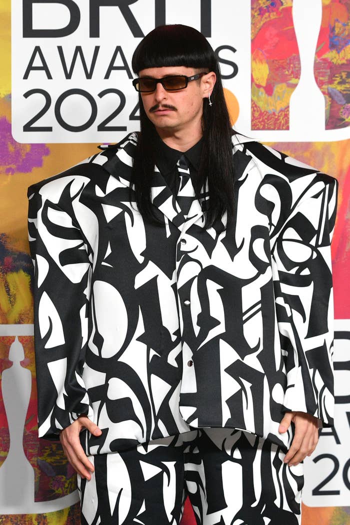Person in oversized, abstract-patterned suit and sunglasses at awards event