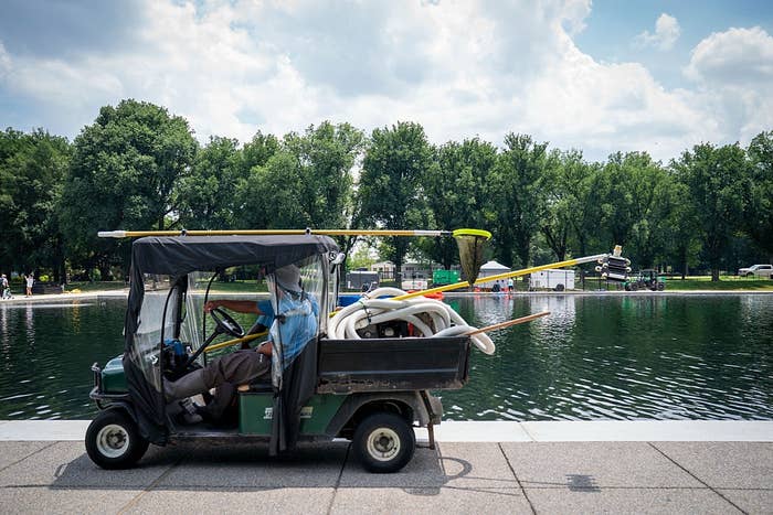 Utility cart filled with excavation  cleaning instrumentality  parked by a ample  pond, surrounded by trees, nether  a partially  cloudy sky