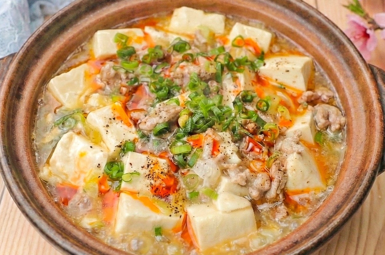 土鍋に入った麻婆豆腐。豆腐、ひき肉、ネギがのった料理で、華やかな見た目が特徴。背景に桜の花が見える。