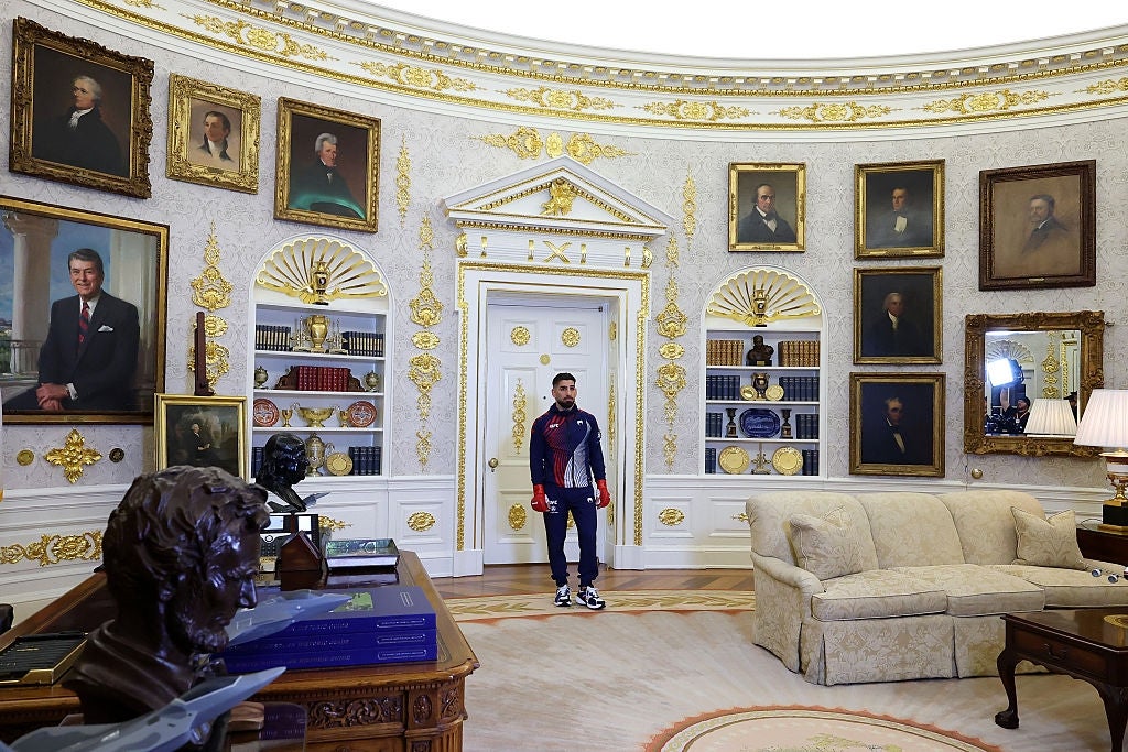 A idiosyncratic stands successful a ceremonial bureau with historical portraits and elaborate decor, wearing a casual tracksuit and sneakers