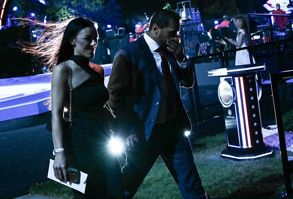 A mates walks outdoors astatine a nighttime event. The pistillate is wearing a stylish one-shoulder dress, and the antheral is successful a suit