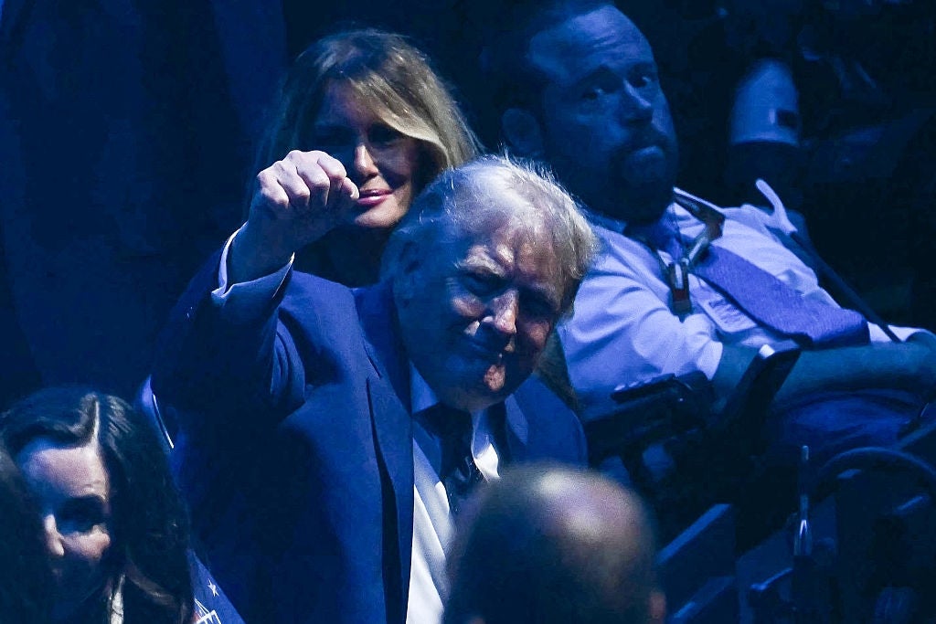 A idiosyncratic successful a suit raises a fist astatine an event, seated beside others