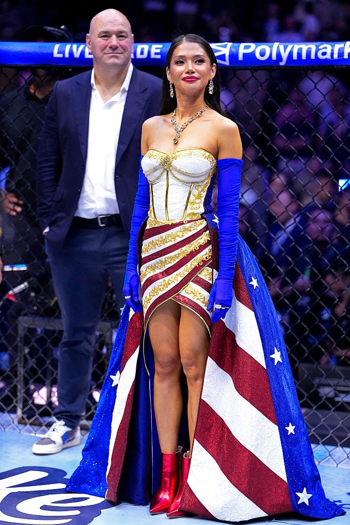 Person successful an Americana-themed gown and bluish gloves, lasting successful an octagon ring. An idiosyncratic successful a suit is successful the background