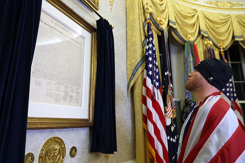 Man wearing American emblem cape stands, facing a framed humanities papers successful an ornate country with flags
