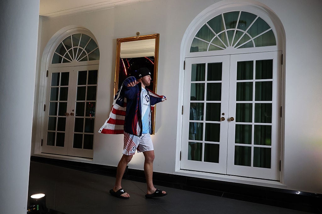 Person walks down a corridor wearing a overgarment with an American emblem design, shorts, and sandals