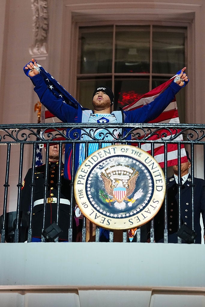 A idiosyncratic stands connected a balcony with arms raised, wearing a flag-themed outfit, surrounded by radical successful ceremonial uniforms
