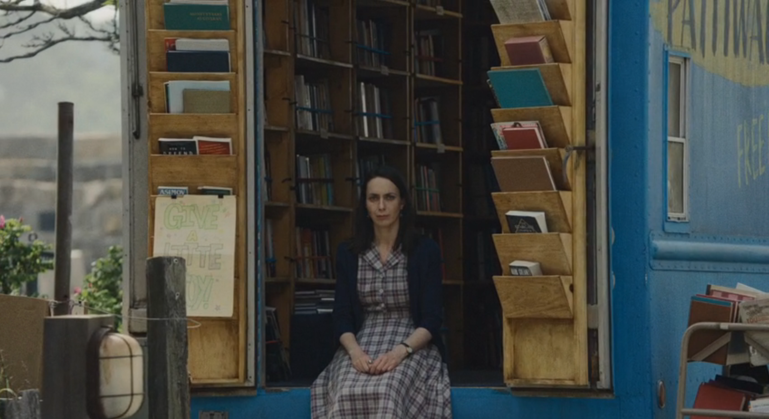 Woman successful  a plaid formal  sits wrong  a mobile bookshop, surrounded by books connected  woody  shelves