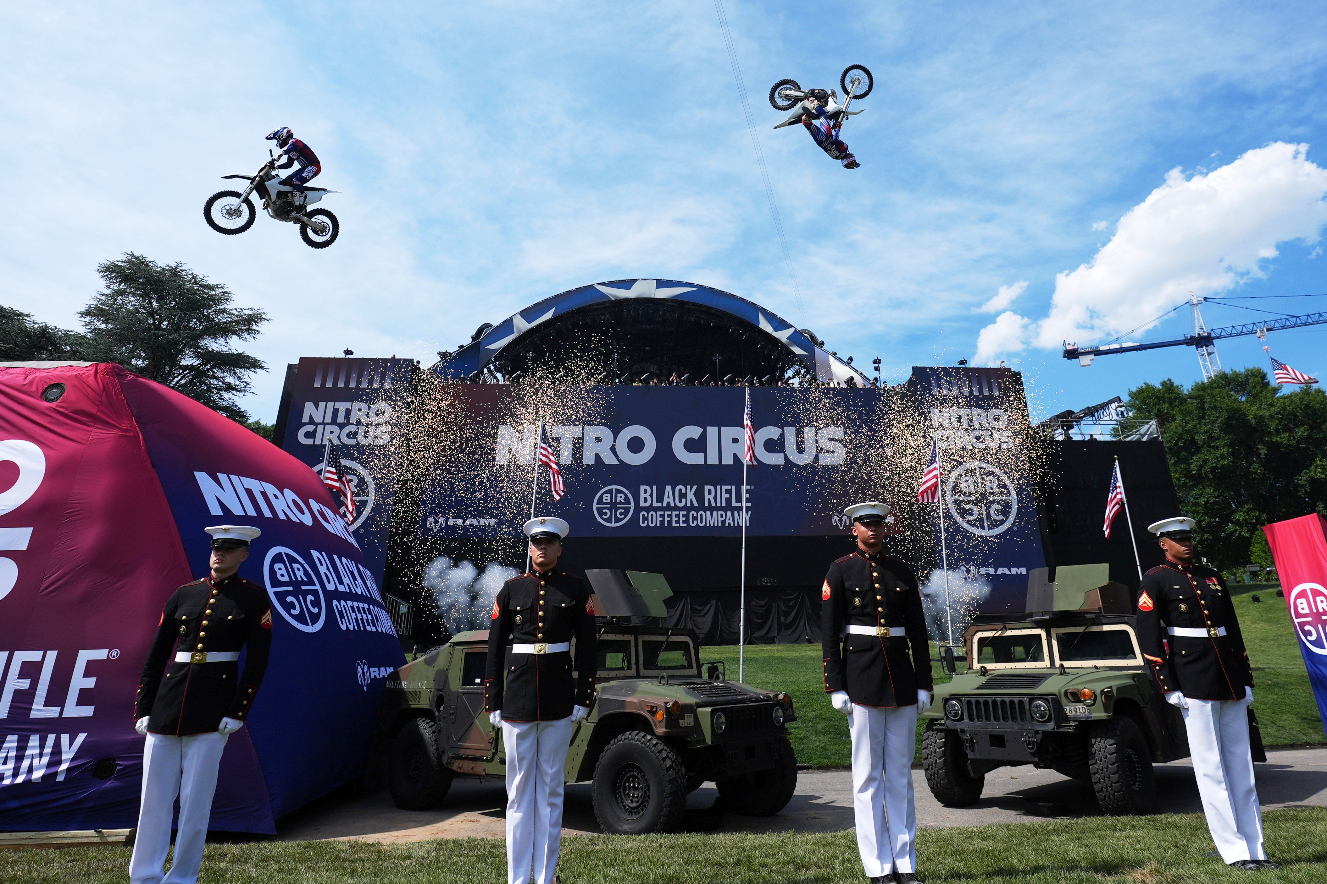 Stunt motorcyclists execute mid-air tricks astatine a Nitro Circus event, with subject unit and vehicles successful the foreground