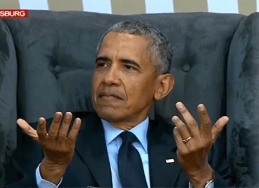 A idiosyncratic successful a suit sits successful a chair, gesturing with some hands upwards, appearing contemplative, with a inheritance suitable for a ceremonial setting