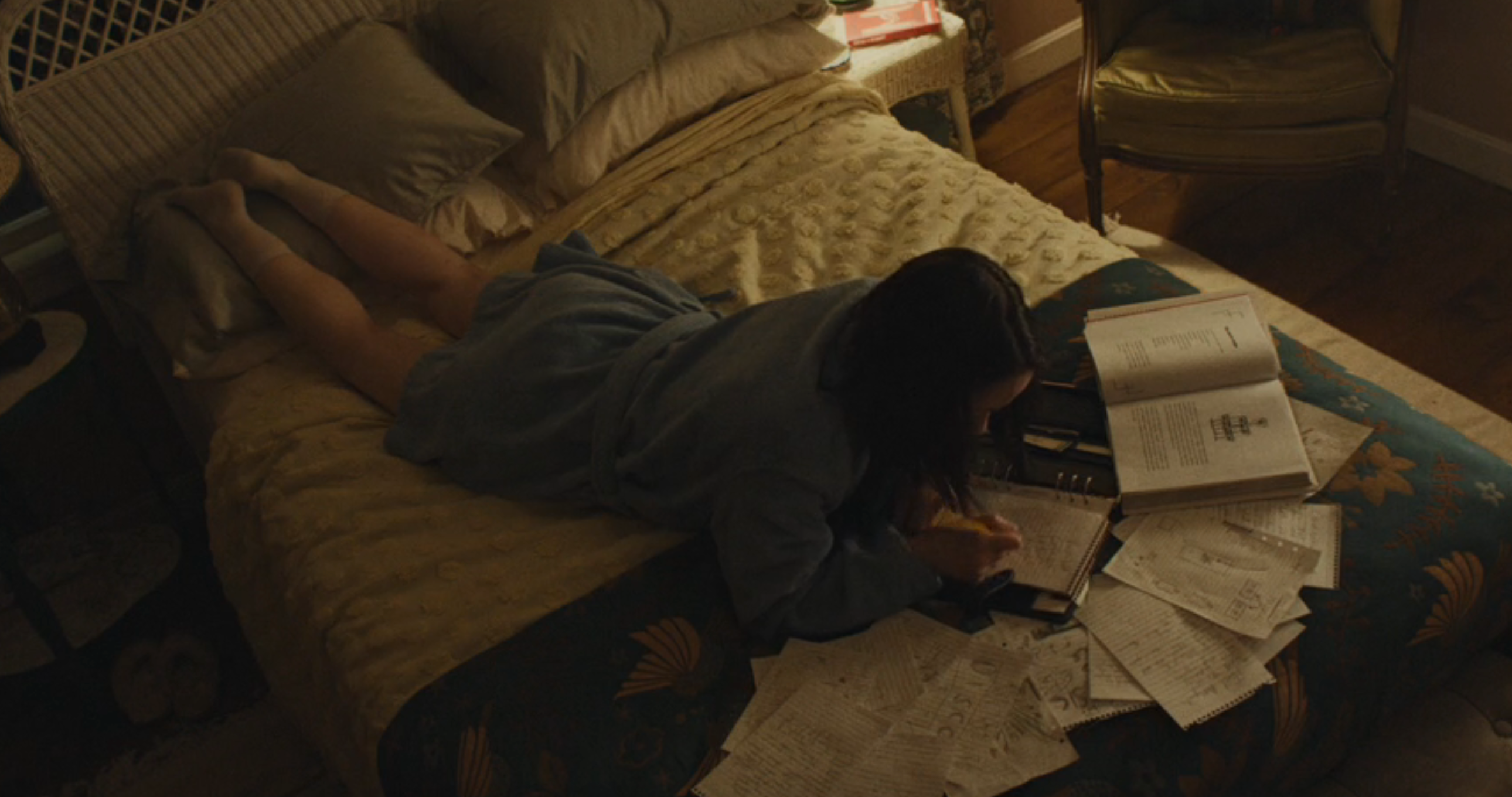 Person lying connected  a furniture  successful  a robe, surrounded by unfastened  books and scattered papers, penning  notes. Room has a seat  and pillows
