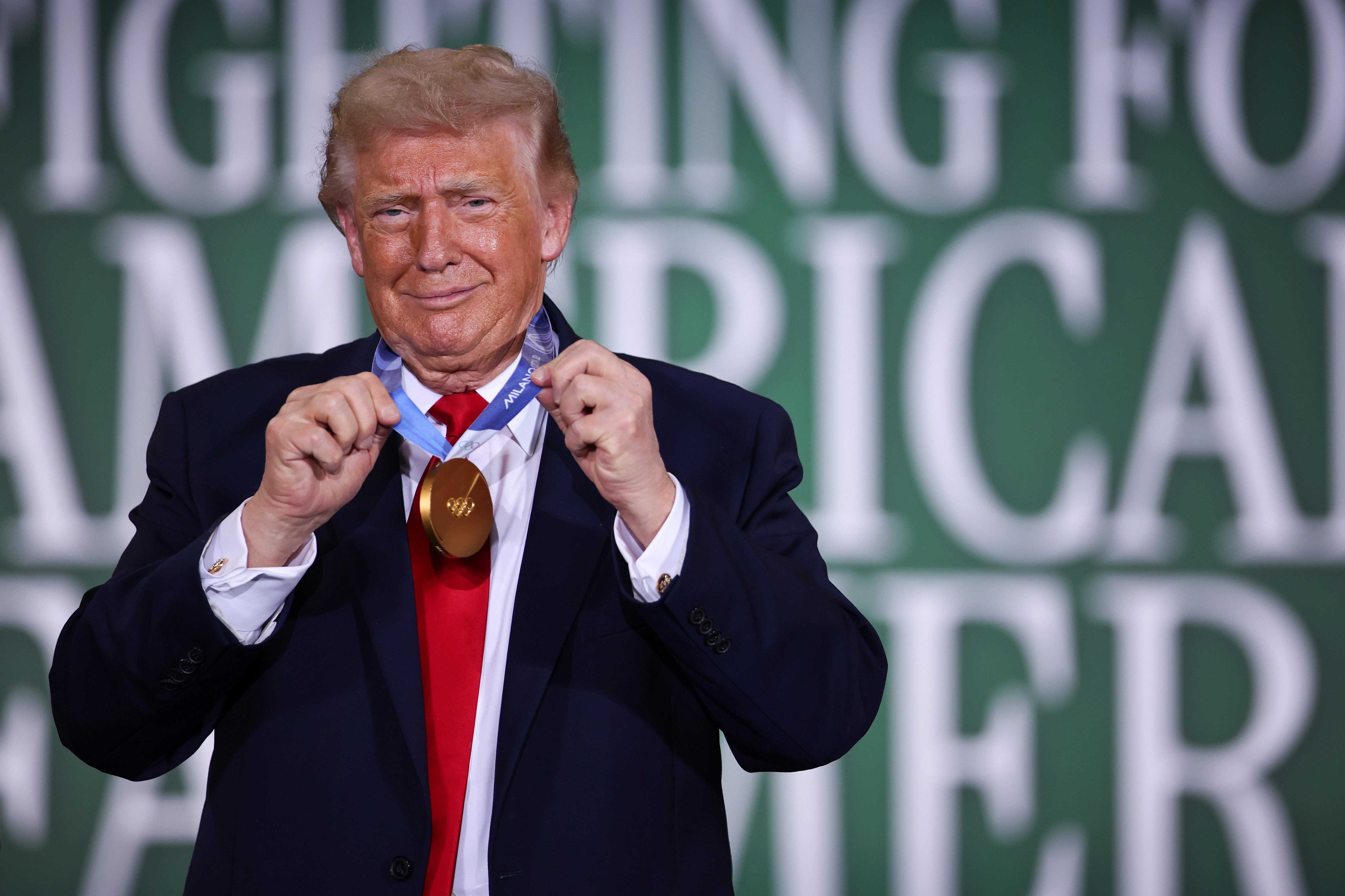 Man successful a suit holding a medal astir his neck, with a backdrop featuring ample text