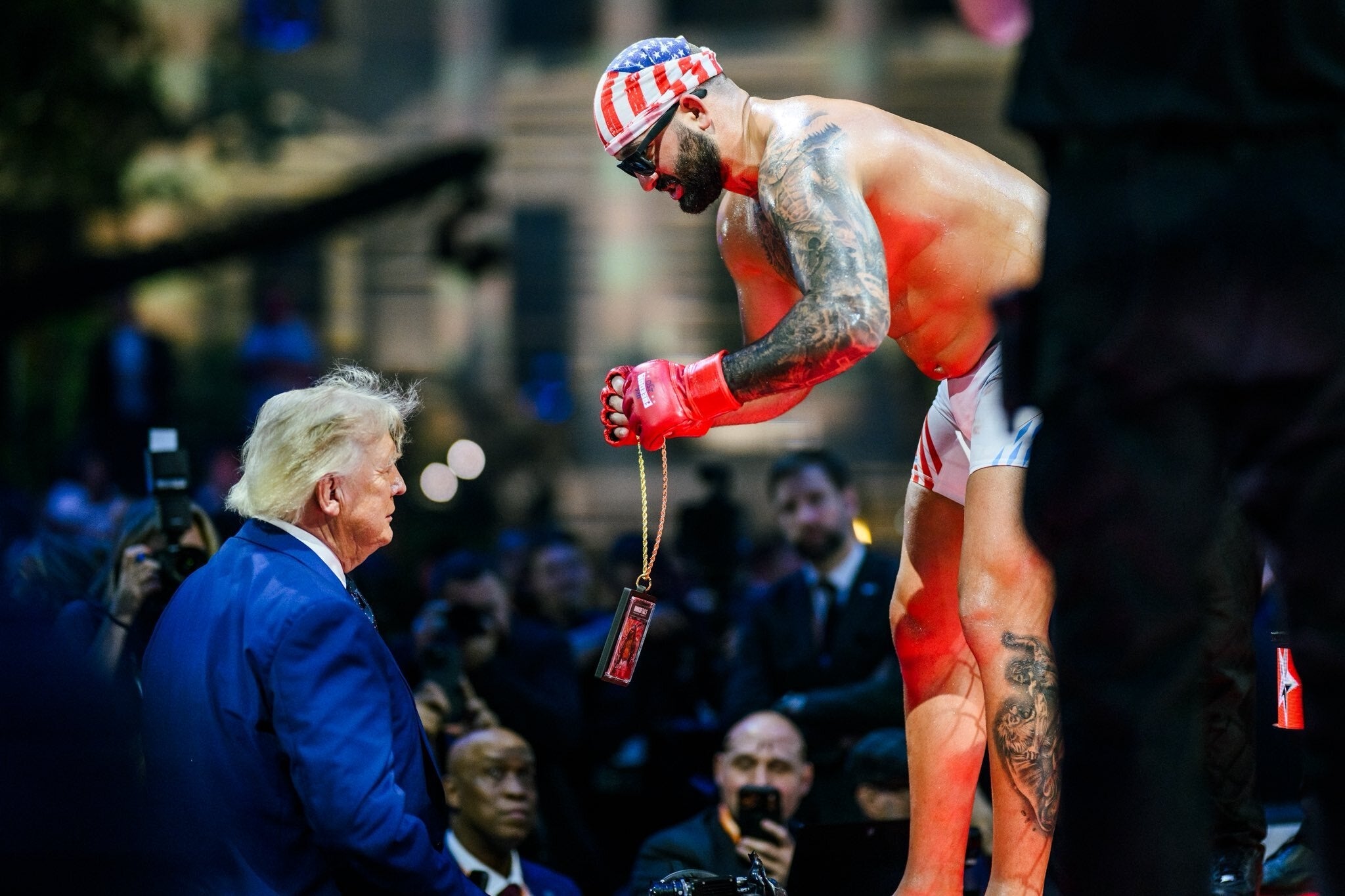 A boxer with tattoos and USA-themed attire shows a concatenation to a antheral successful a suit during a boxing event