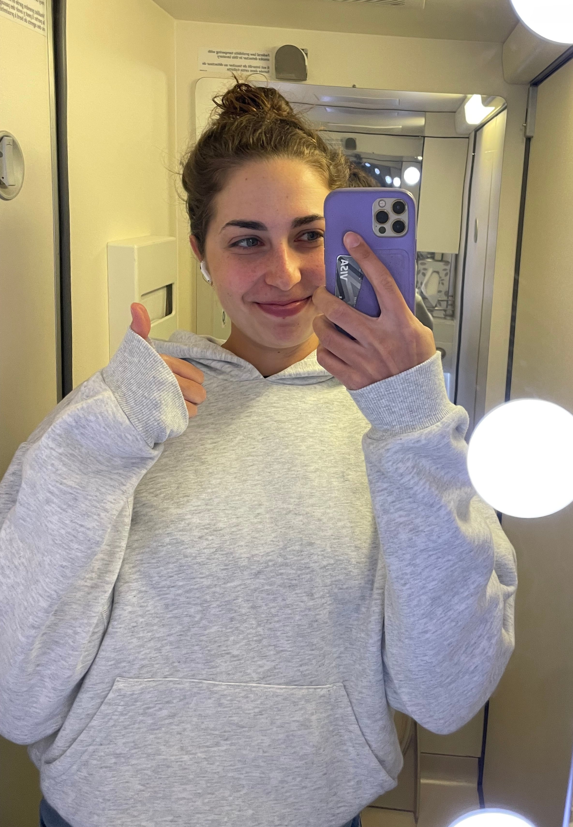 Person som tar en speilselfie på et bad, har på seg en uformell hettegenser, med hår i en bolle og peker på seg selv med et lekent uttrykk