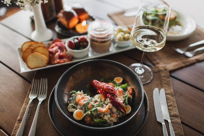 A gourmet repast  featuring a seafood crockery  with a lobster connected  top, surrounded by tiny  quail eggs and herbs, accompanied by a solid  of achromatic  wine