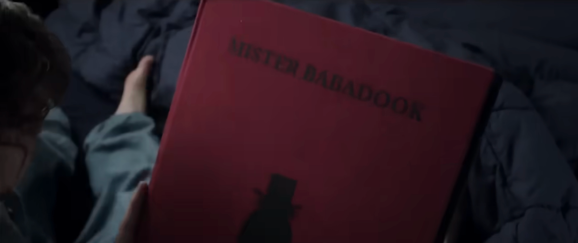 A idiosyncratic   holds a publication  titled "Mister Babadook," featuring an illustration of a top-hatted figure