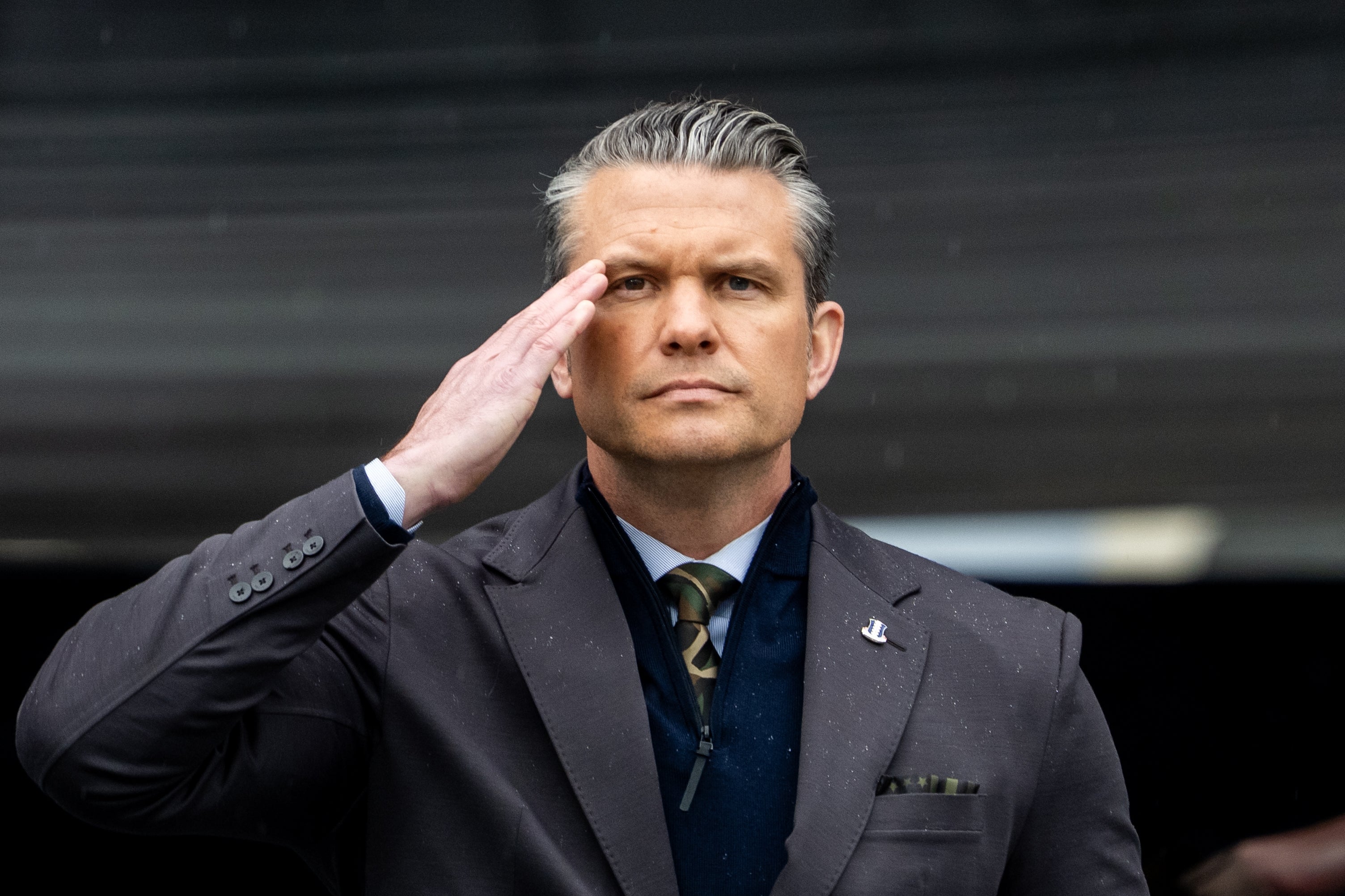 Person i formell dress som hilser, ser alvorlig ut, satt mot en uskarp bakgrunn, vises i en nyhetsrelatert artikkel