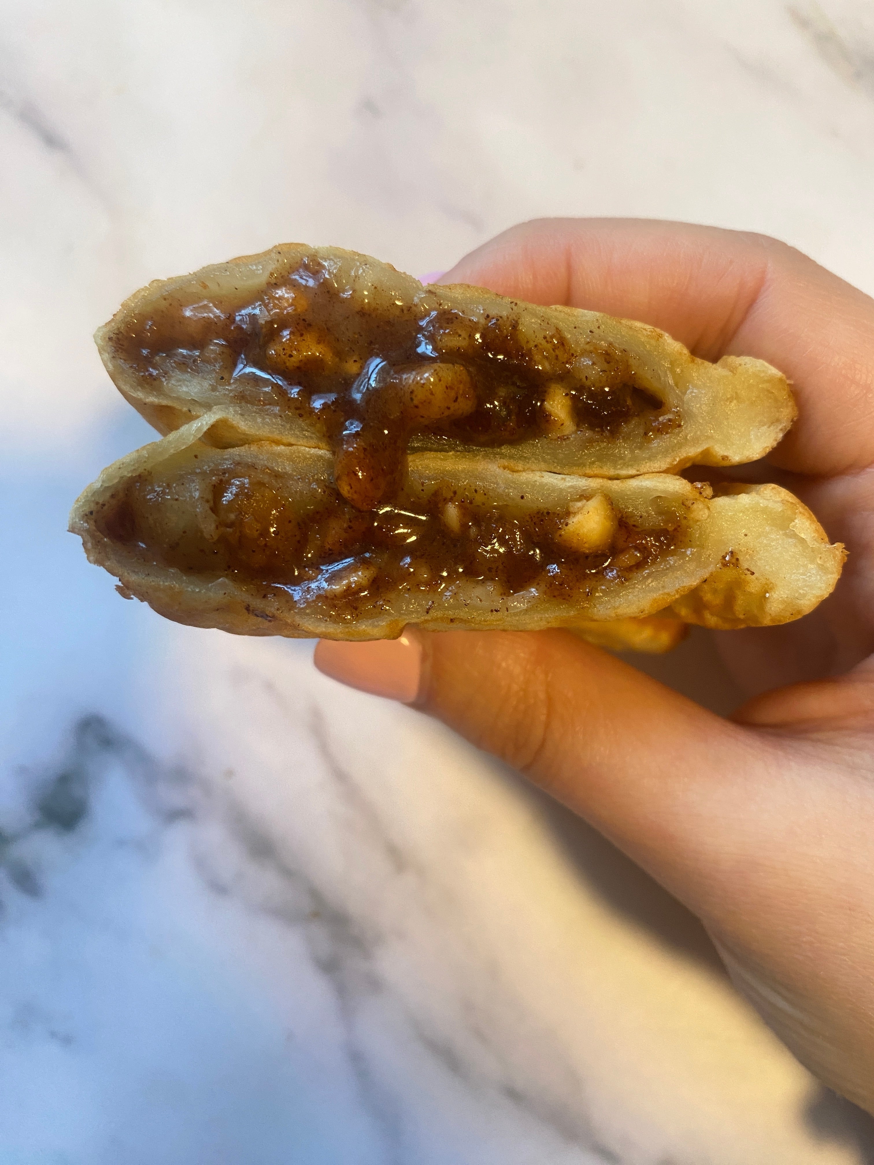 A hand holds a sliced waffle with gooey filling, likely containing nuts and syrup, highlighting its indulgent, tasty interior