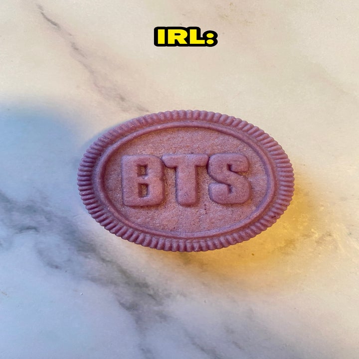 A cookie with "BTS" embossed on it lies on a marble surface