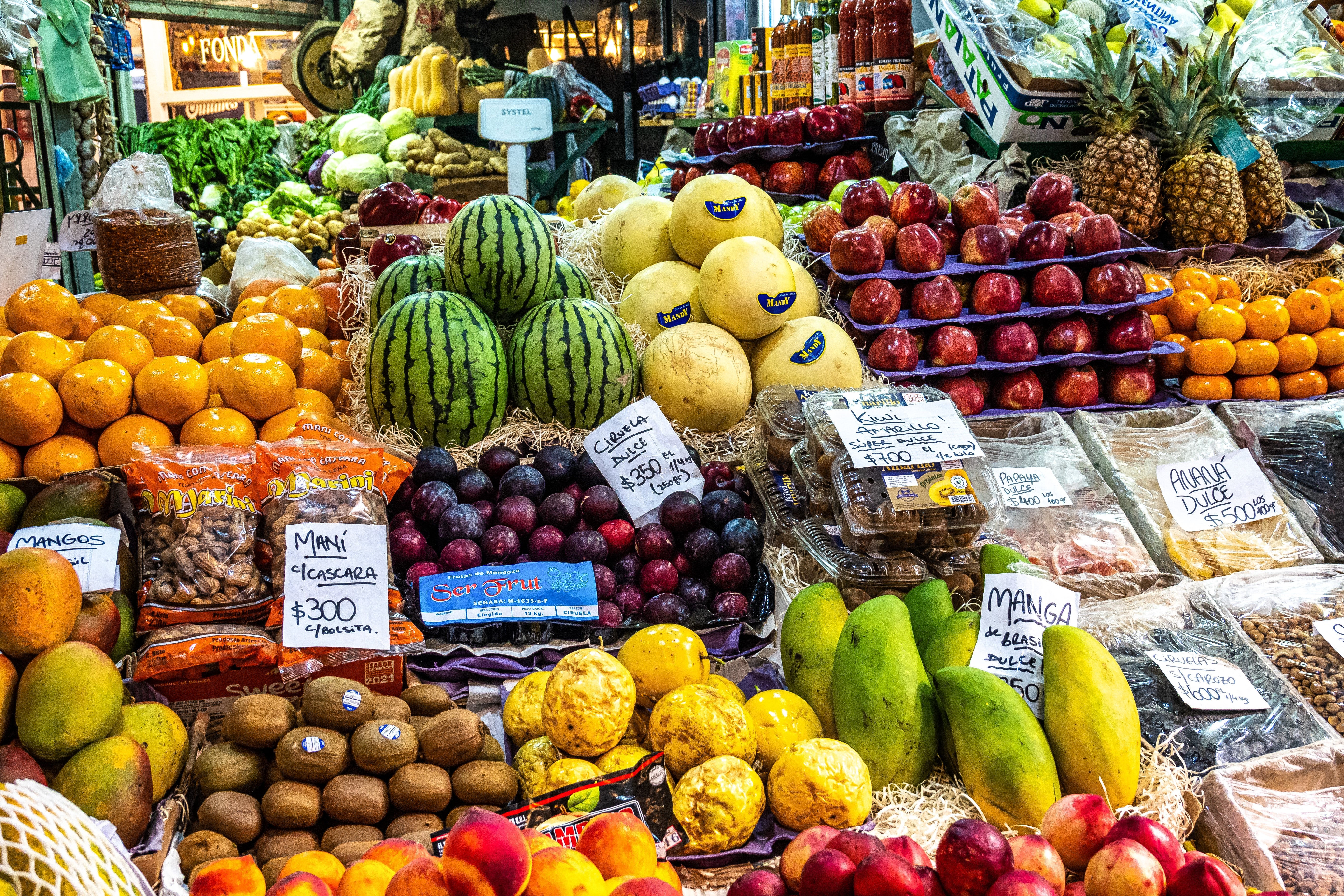 An array of fruits and vegetables connected a vibrant marketplace stand, featuring melons, oranges, kiwis, and pineapples, with terms tags displayed