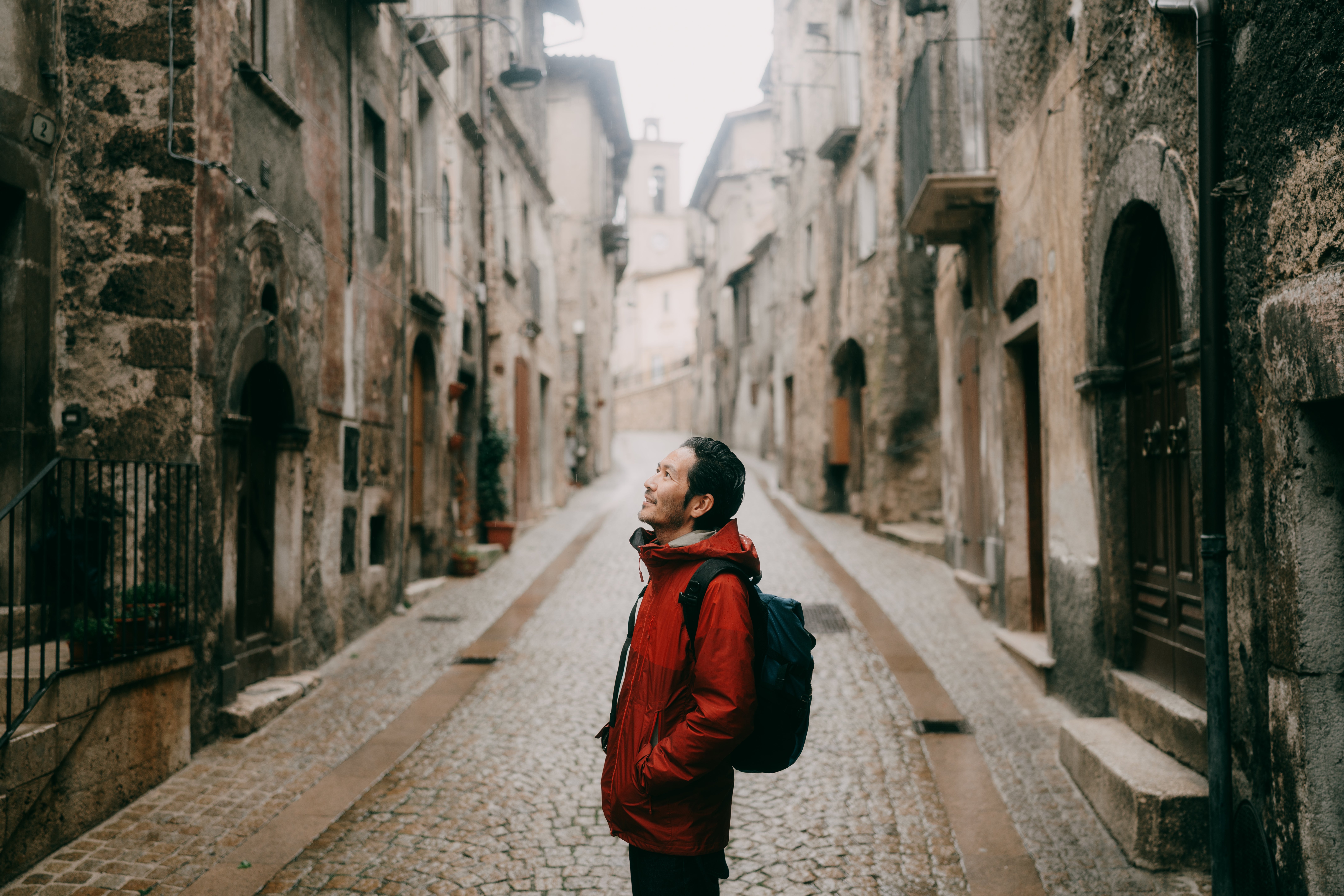 Person successful a cobblestone thoroughfare looking up astatine historical chromatic buildings, wearing a backpack and casual jacket, evoking a consciousness of exploration