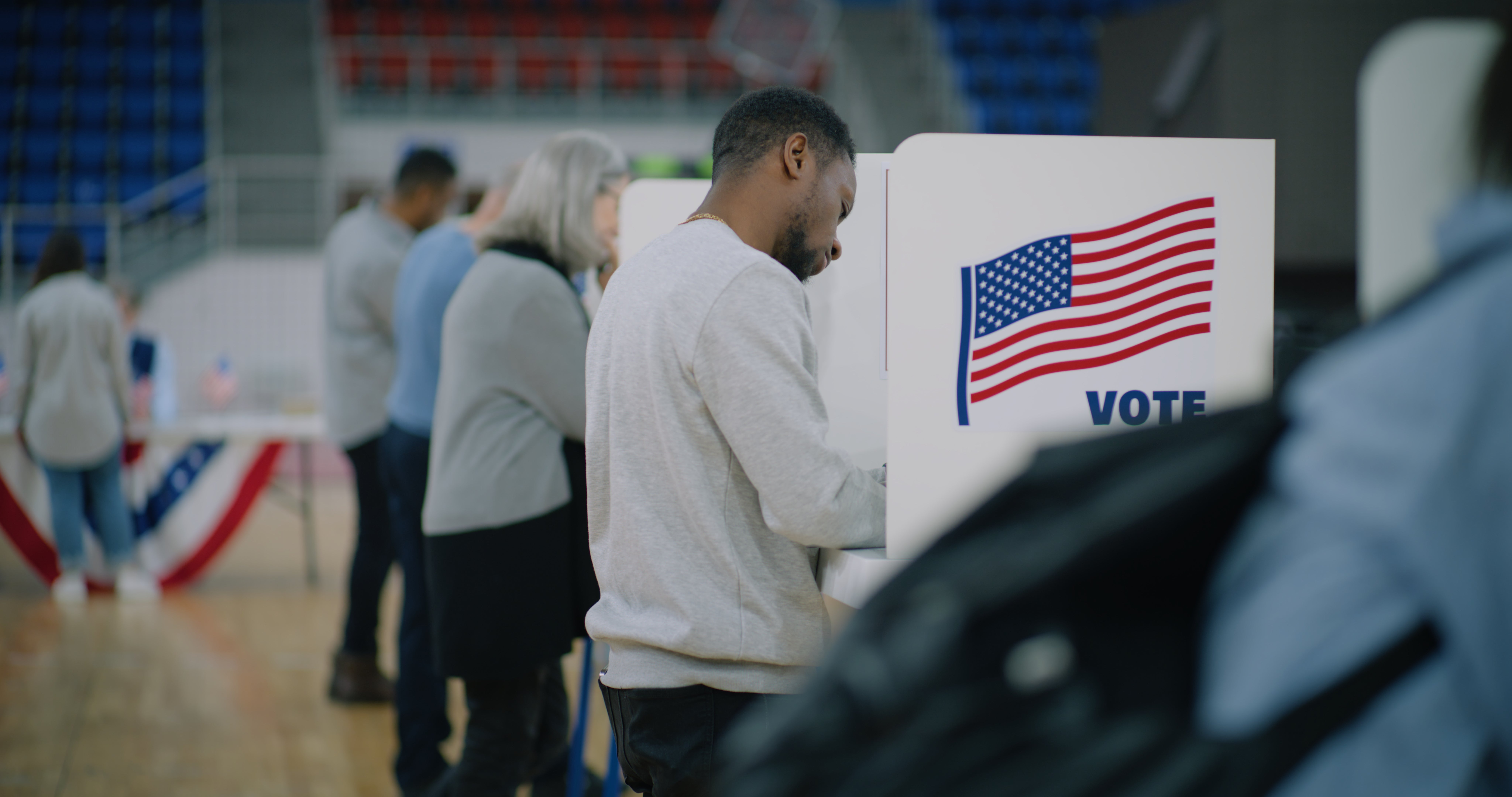 Folk som står i kø og stemmer ved båsene med et amerikansk flagg og ordet 