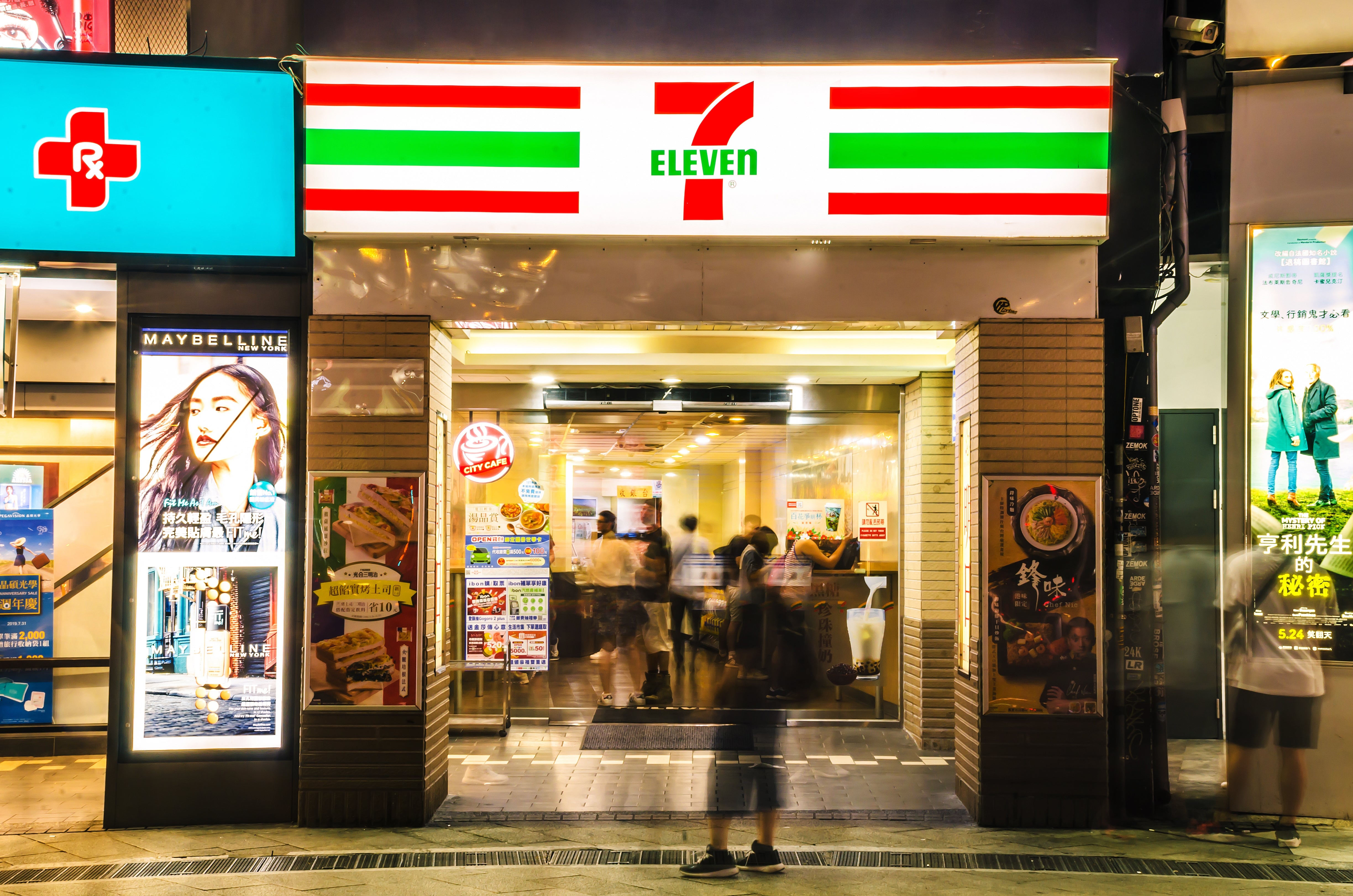 People locomotion past a brightly lit 7-Eleven store entranceway astatine night, successful a engaged municipality area