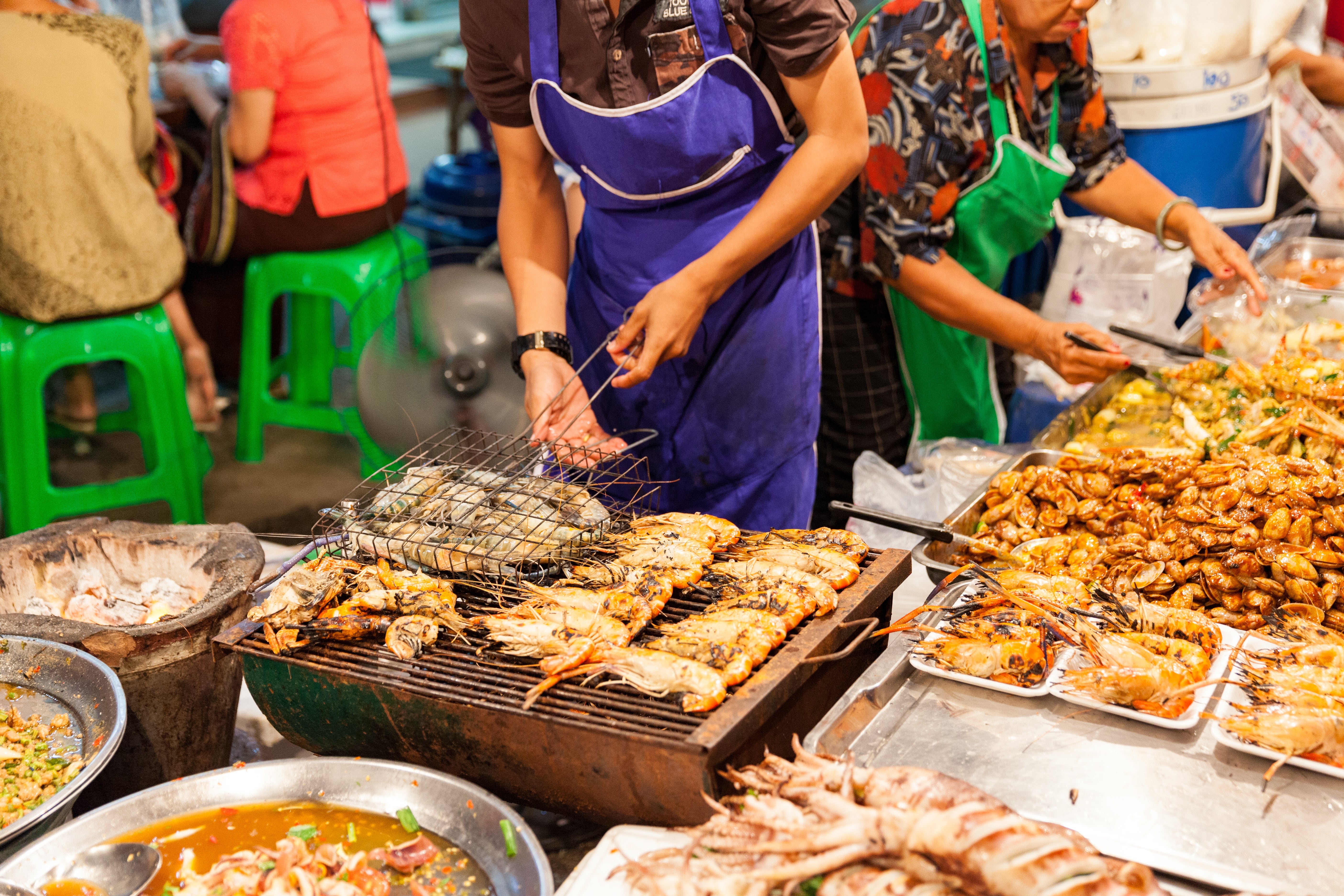 Street vendor grilling seafood and serving assorted dishes astatine a bustling market, with radical seated adjacent enjoying their meals
