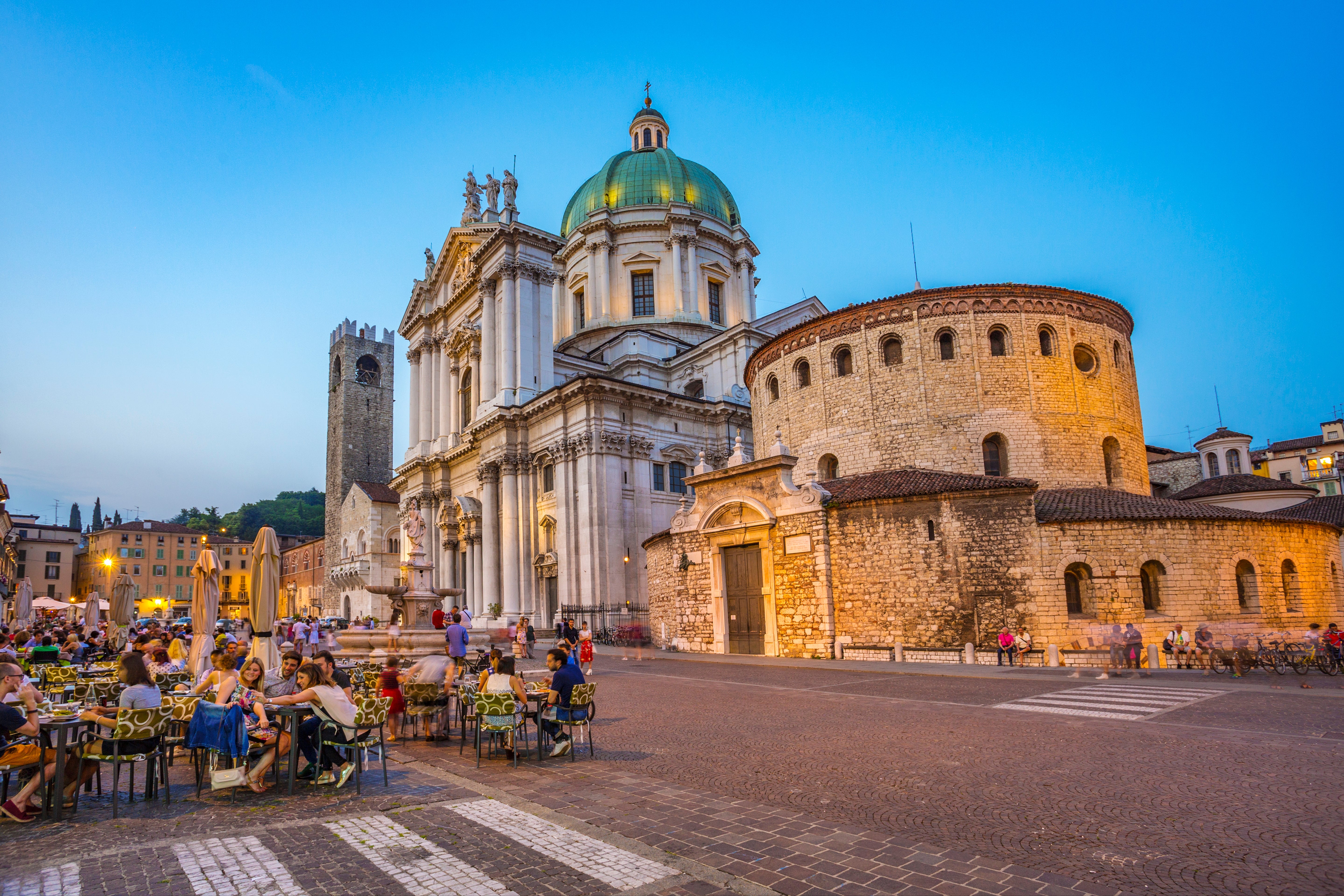 People eating outdoors adjacent the scenic Brescia Cathedral and Rotonda successful Italy, showcasing historical architecture