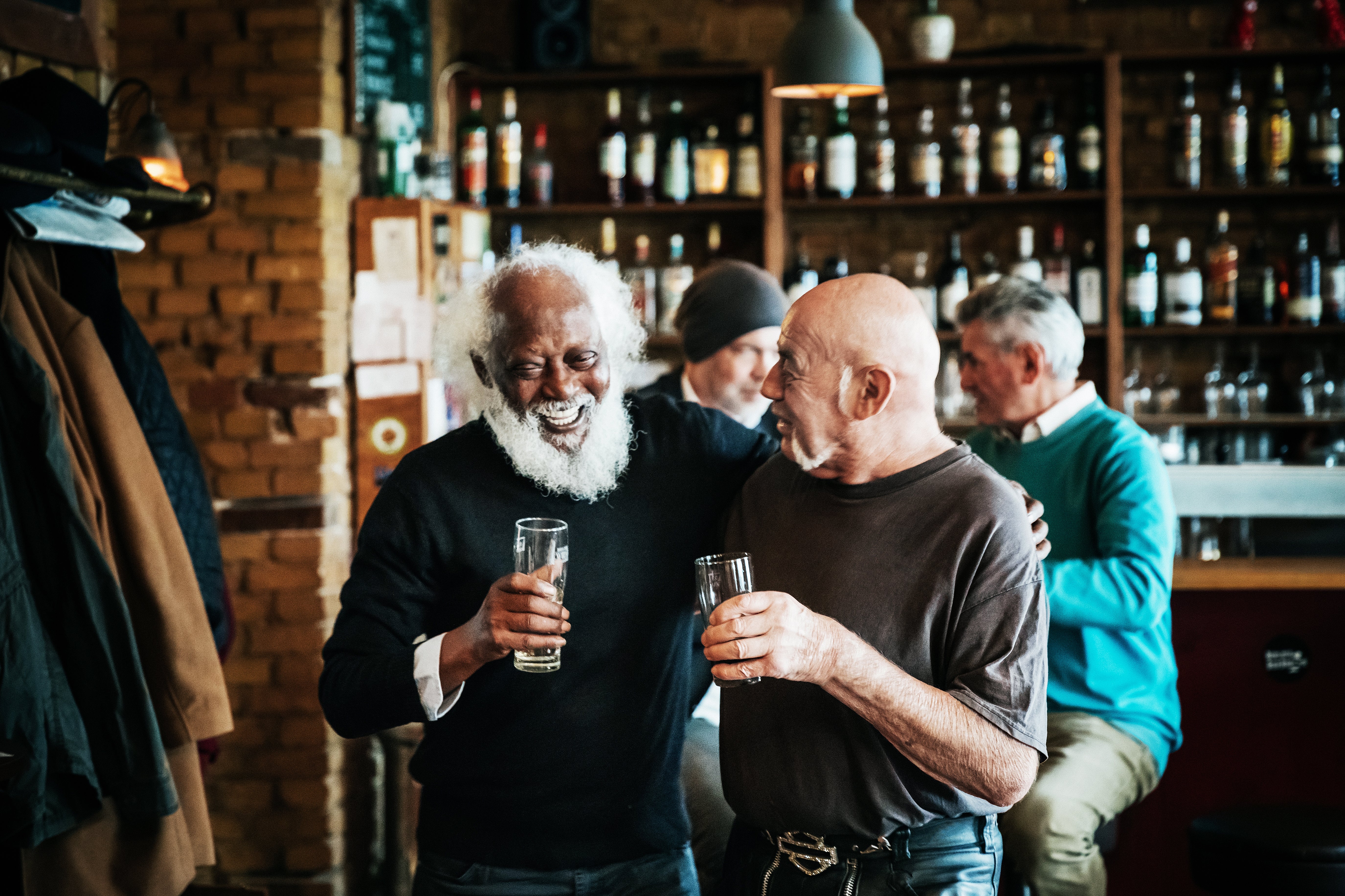 Two men successful a barroom laughter together, each holding a drink. The mounting is casual and lively, with shelves of bottles successful the background