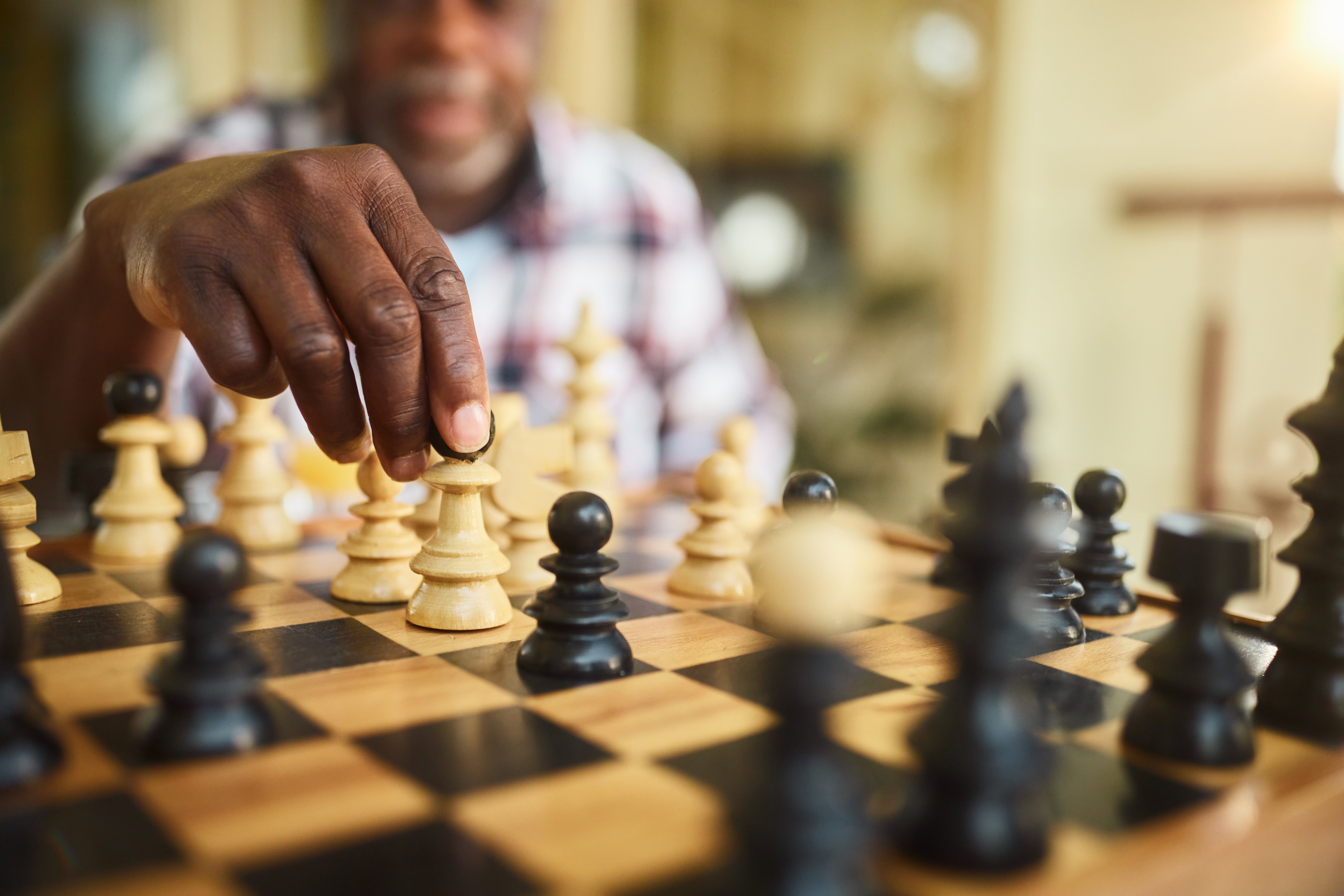 Person playing chess, focused connected moving a knight portion during a game. The chessboard and pieces are successful the foreground