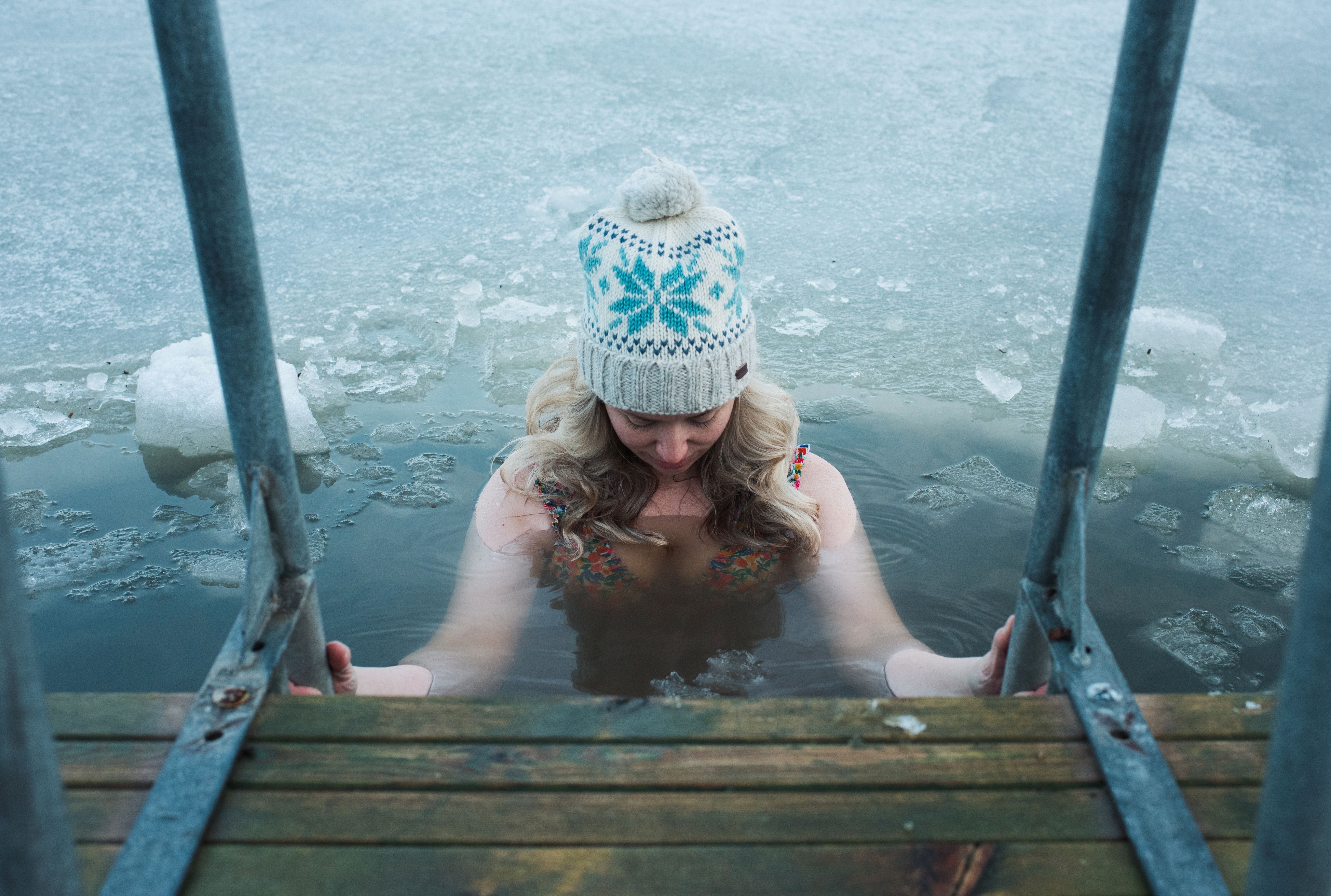 Person successful a knitted chapeau and swimsuit wades successful icy h2o connected a woody dock, surrounded by snowfall and ice