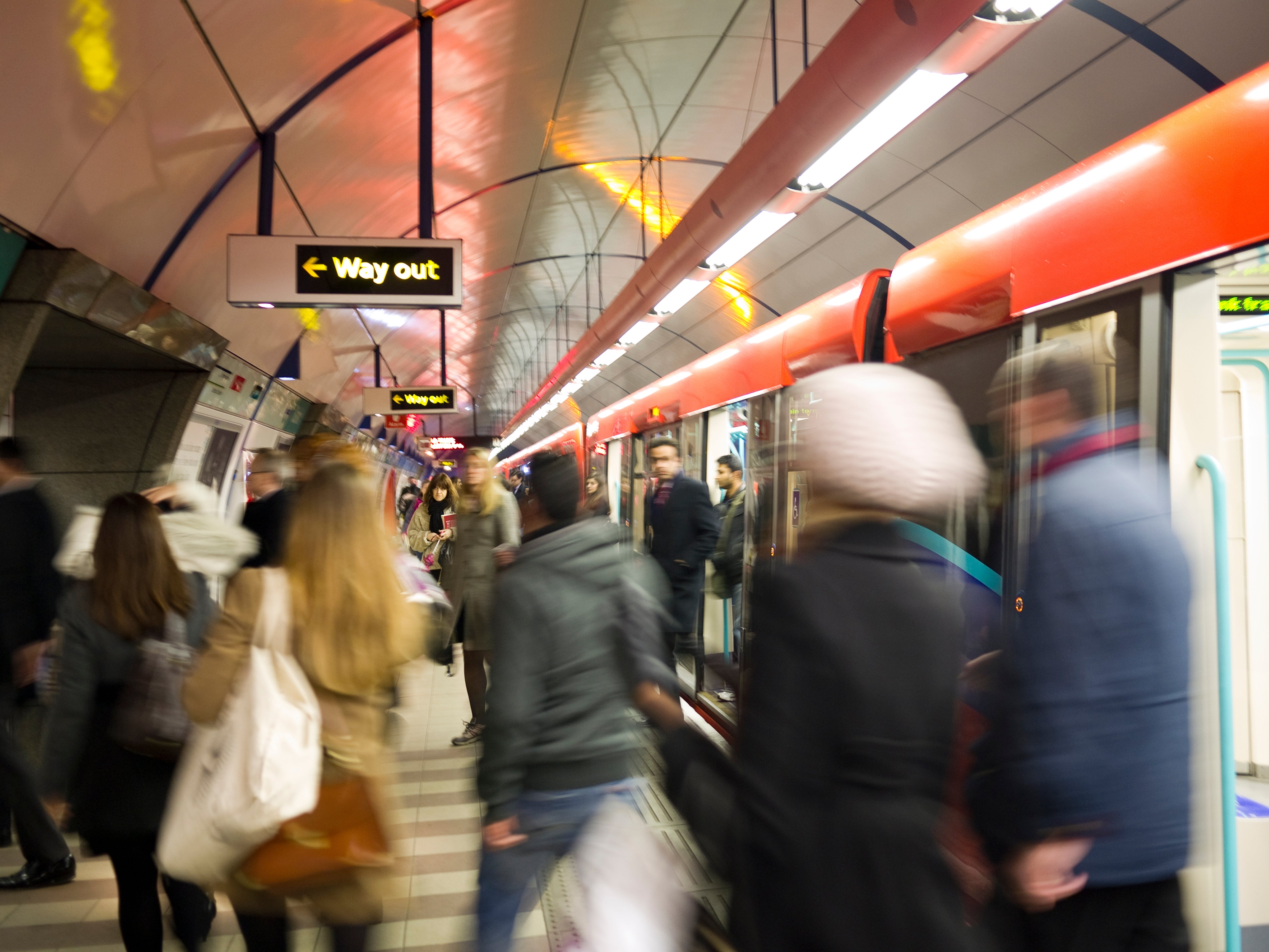 People boarding a engaged bid astatine a modern, bustling subway station. Signs bespeak an exit. Movement suggests an municipality transit environment