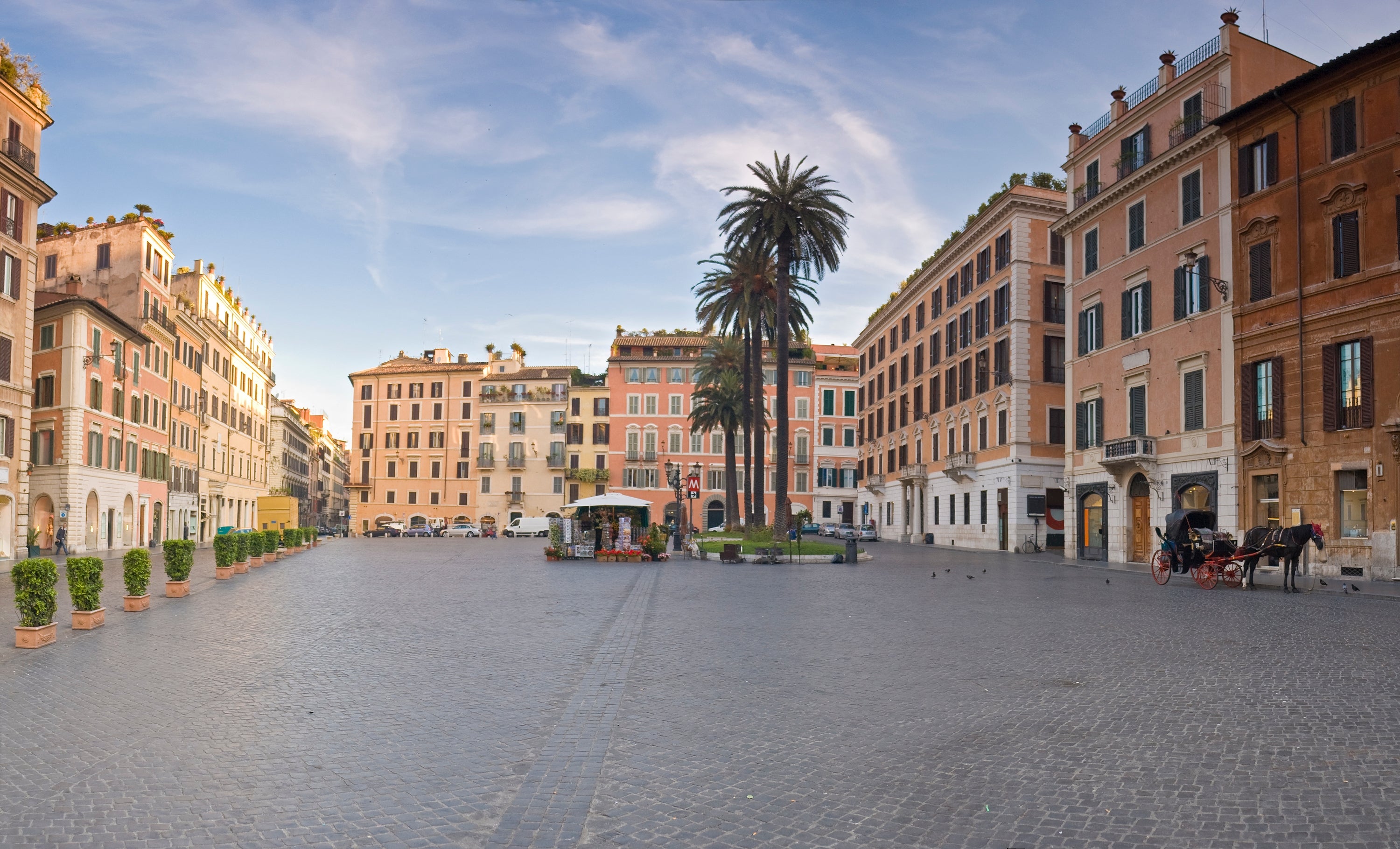 A spacious European plaza with historical buildings, thenar trees, and an bare cobblestone quadrate nether a wide sky