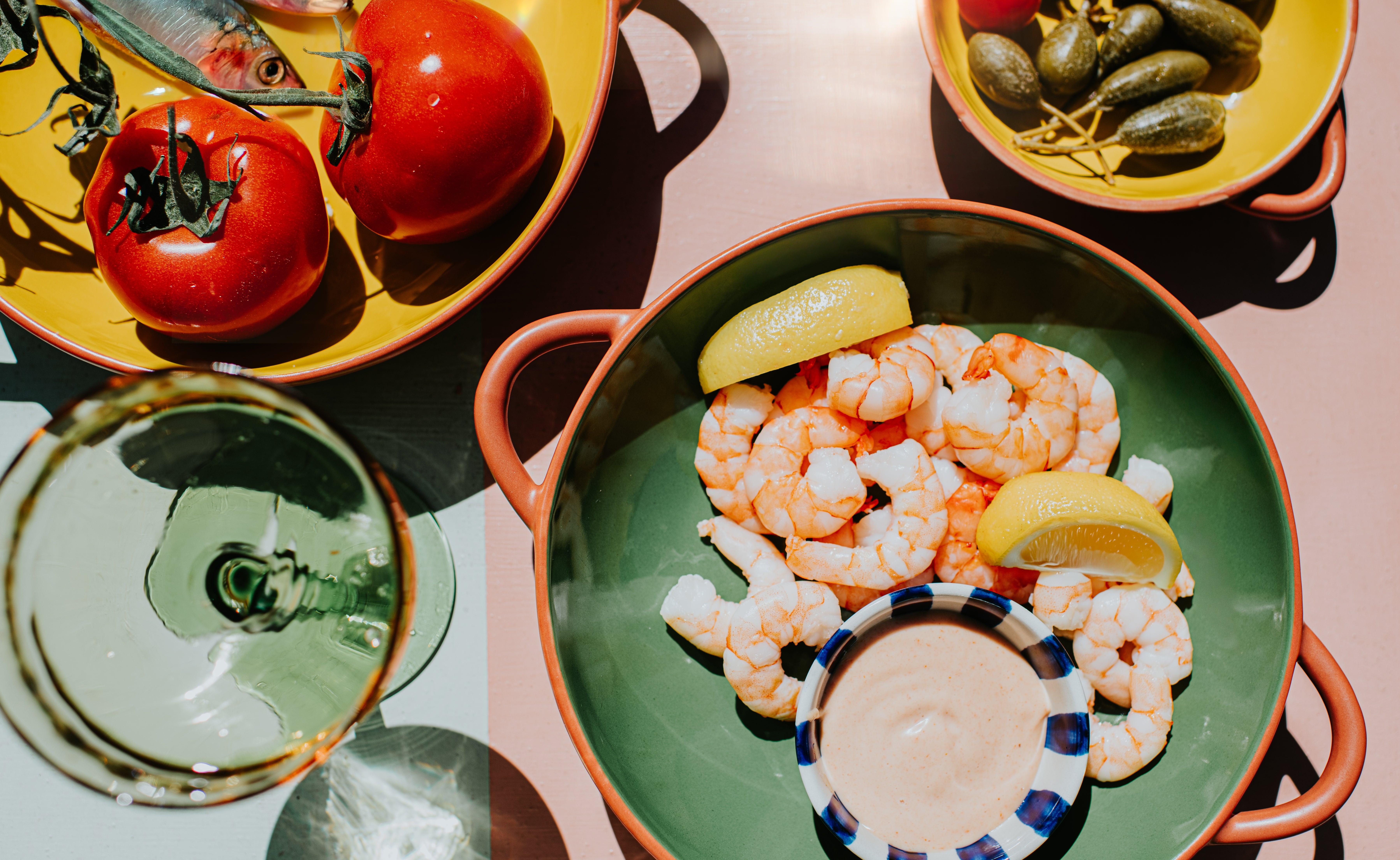 Plates of caller tomatoes, shrimp with citrus and dipping sauce, pickles, and a solid of achromatic vino connected a table