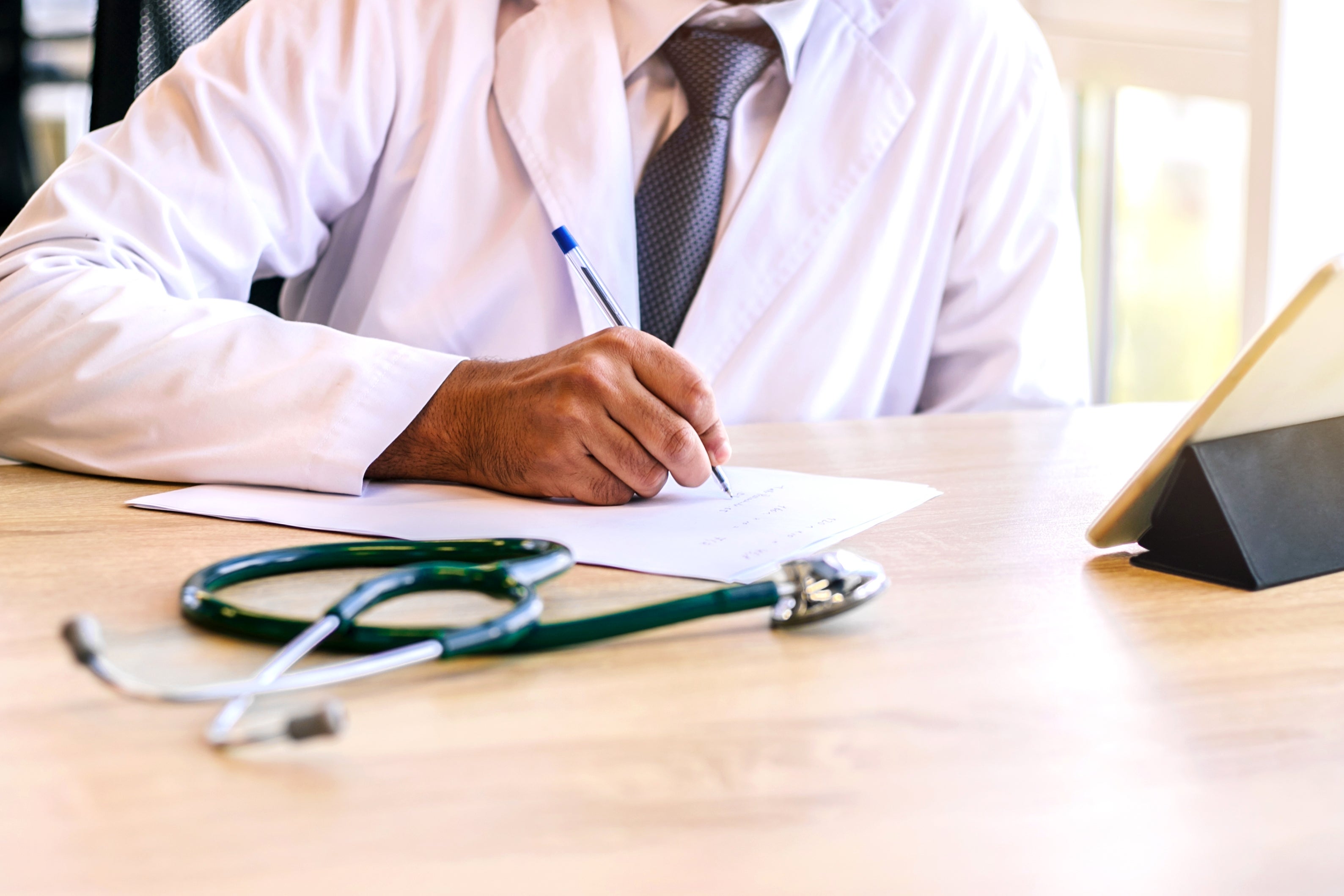 Doctor penning notes astatine a table with a stethoscope nearby