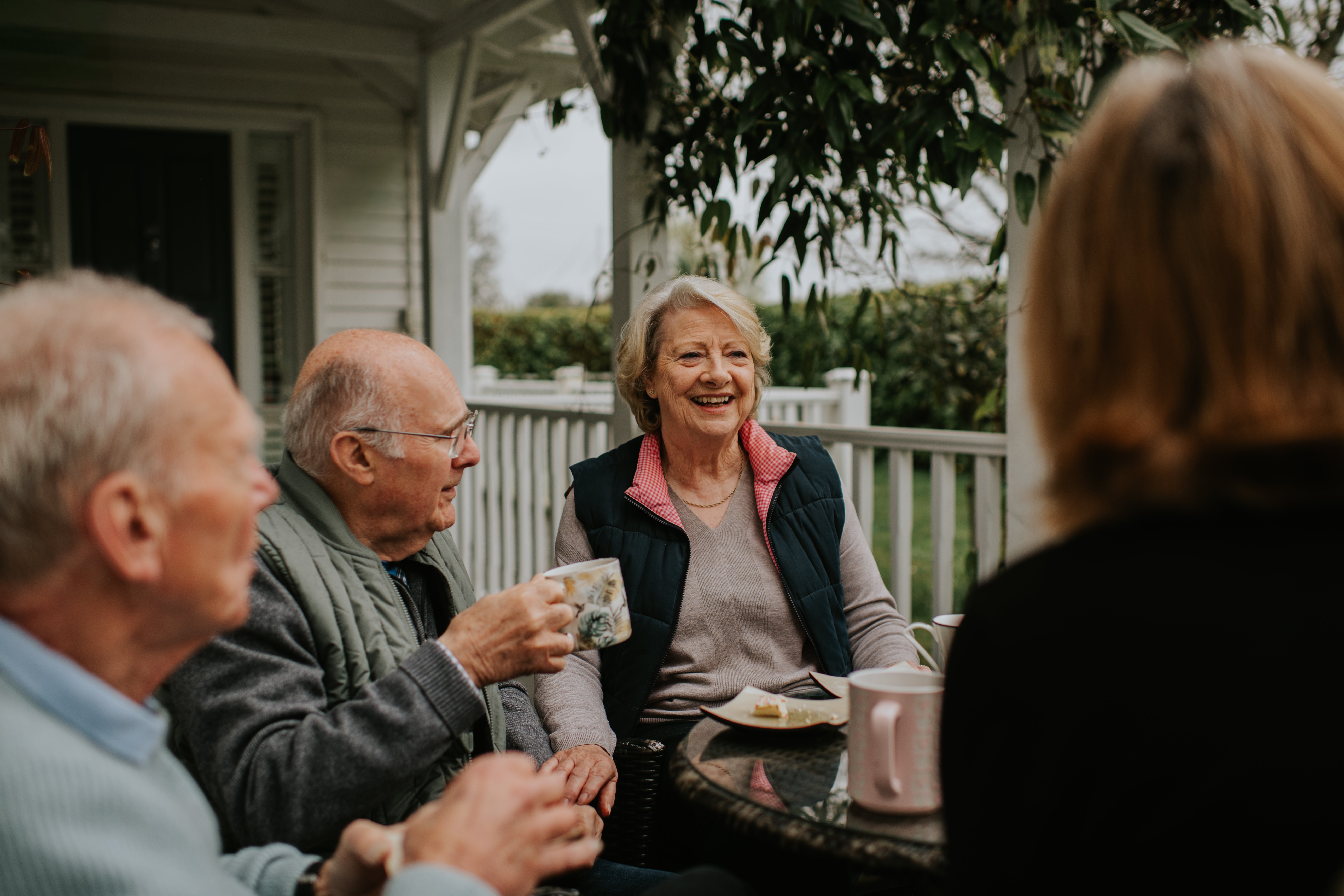 Elderly friends bask java and speech connected a porch, seated astir a array with mugs