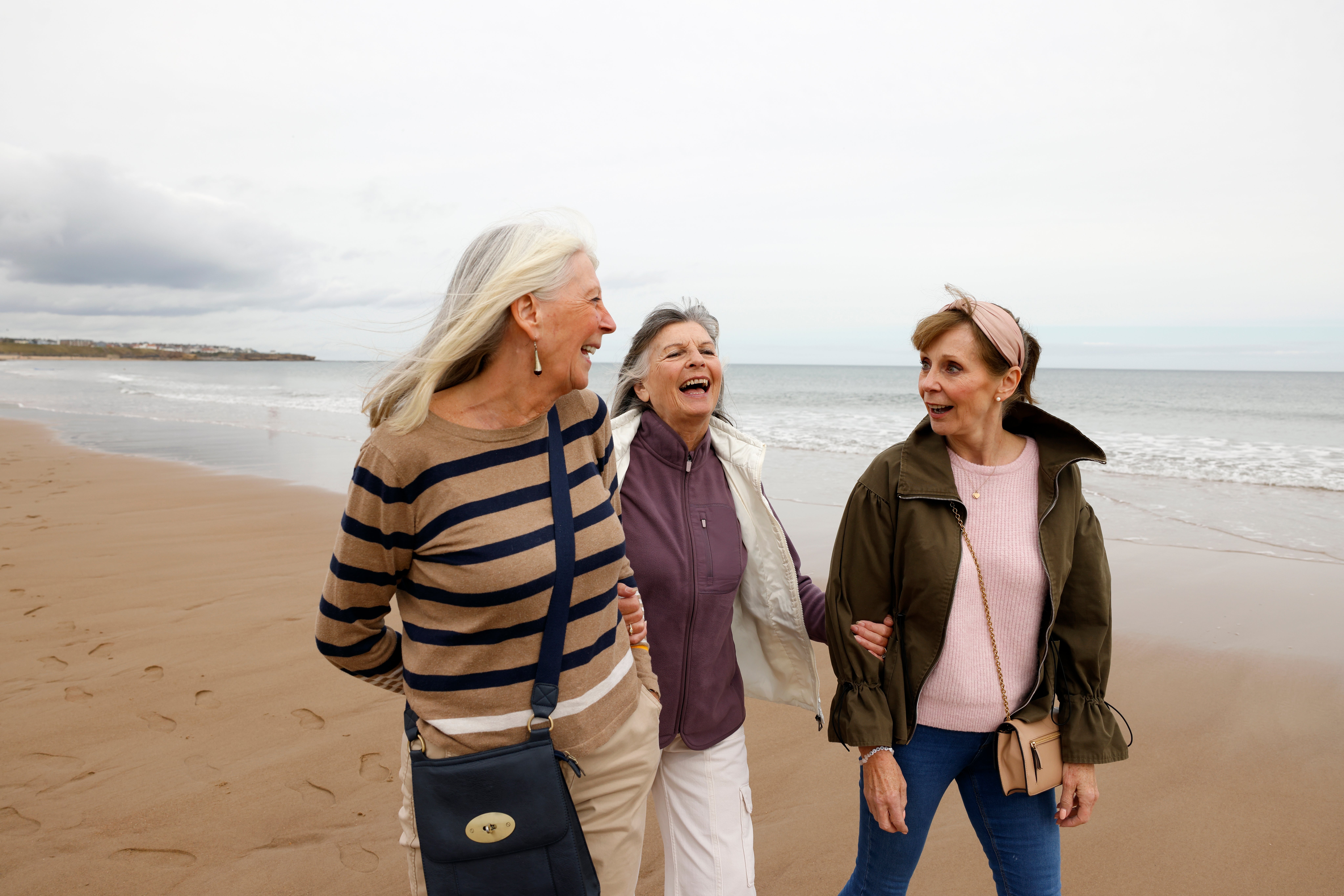 Three women walking unneurotic connected a beach, smiling and chatting, with the water successful the background