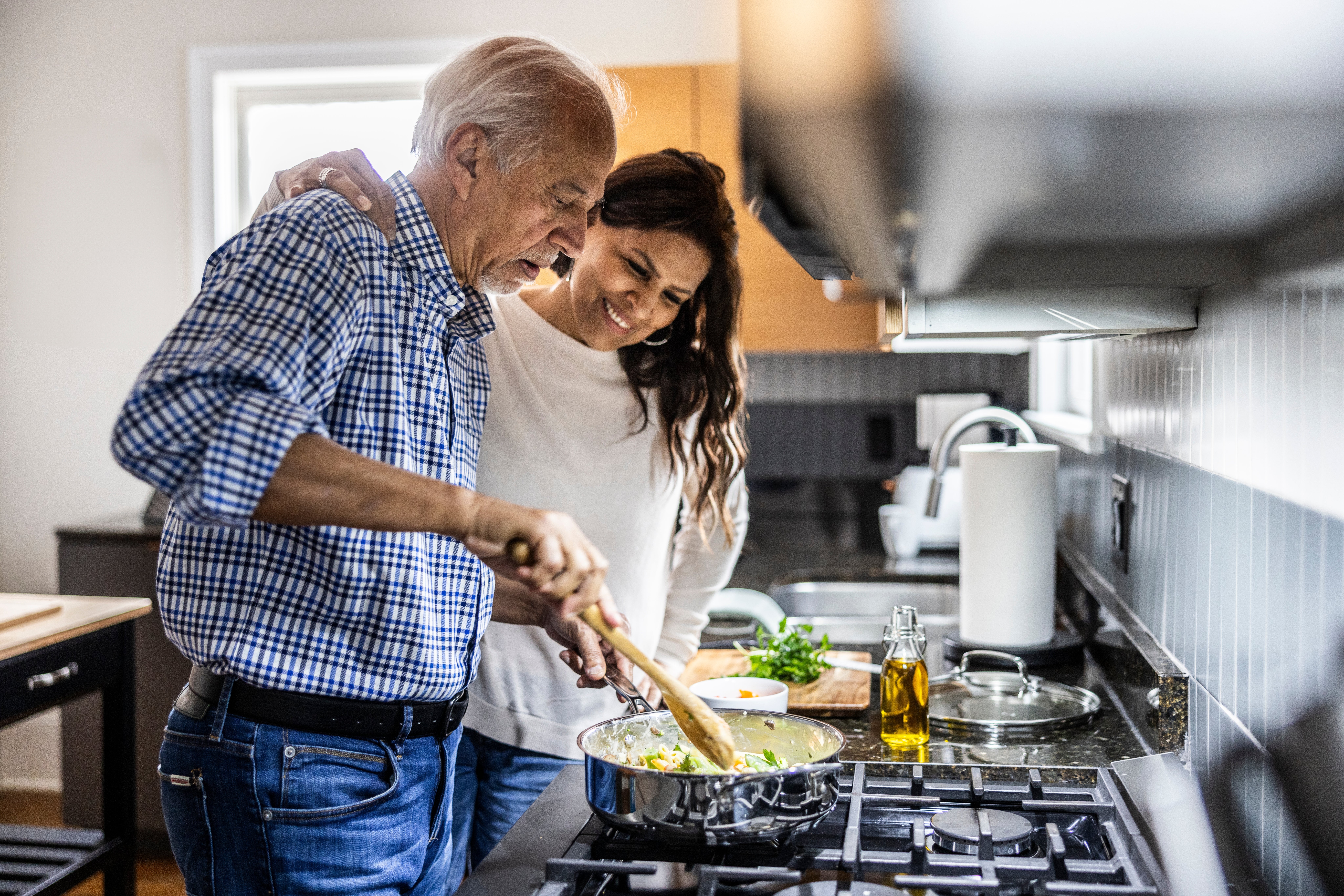 Older antheral and younger pistillate cooking unneurotic successful a modern kitchen, smiling arsenic they disturbance nutrient successful a cookware connected the stove