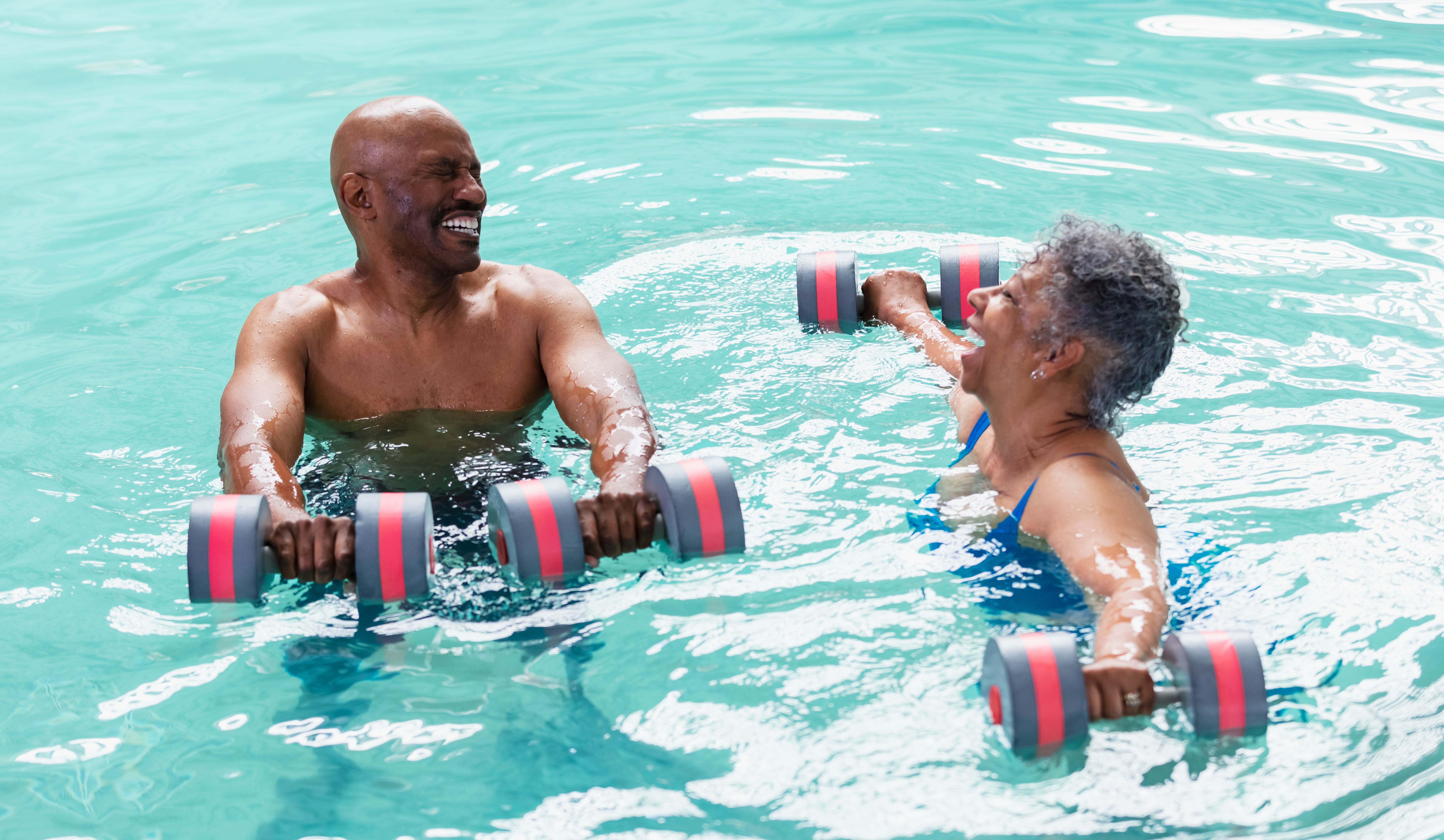 Two older adults successful a excavation smiling and holding dumbbells during a h2o workout class