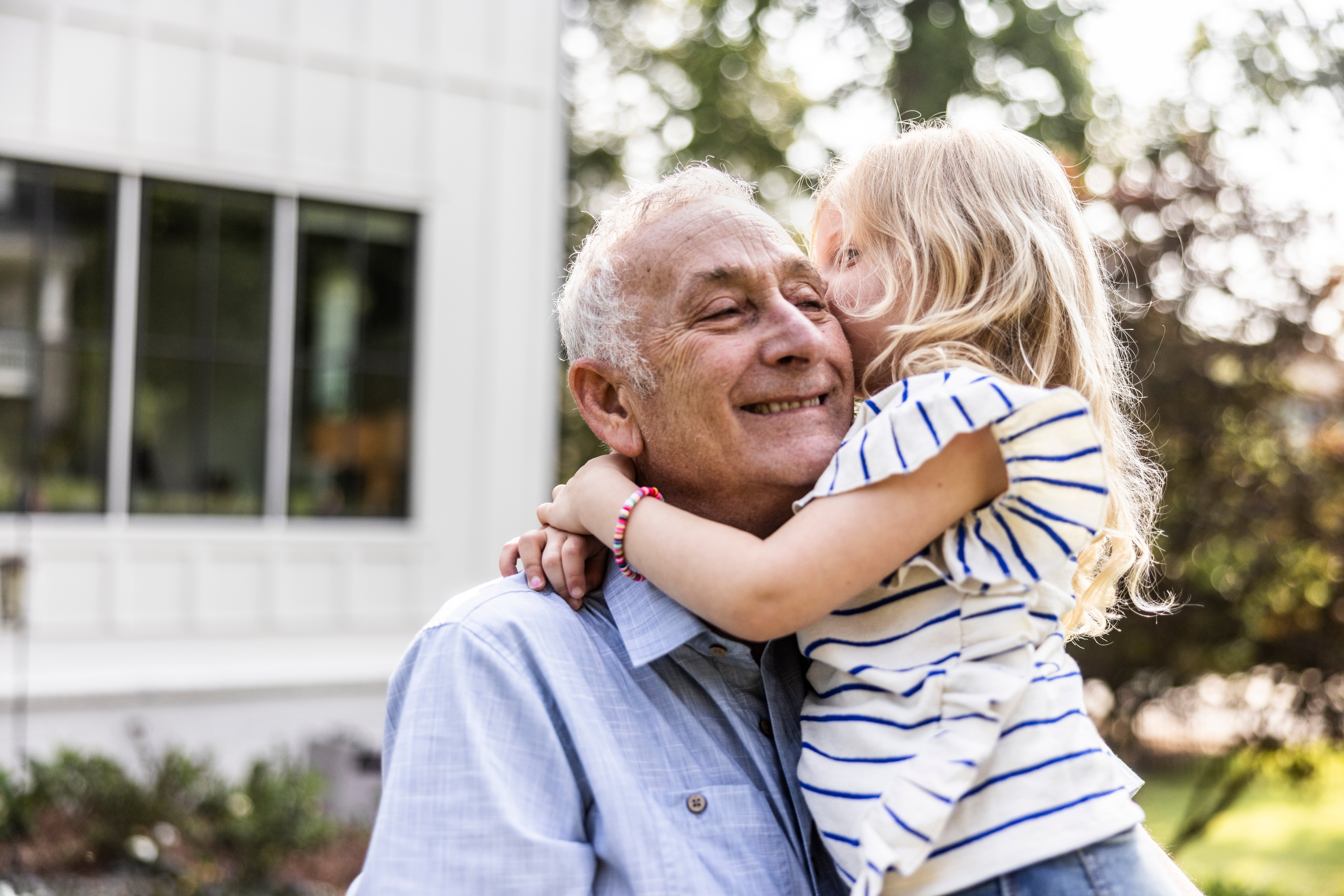 Grandfather smiling arsenic young miss successful striped garment hugs him affectionately outdoors