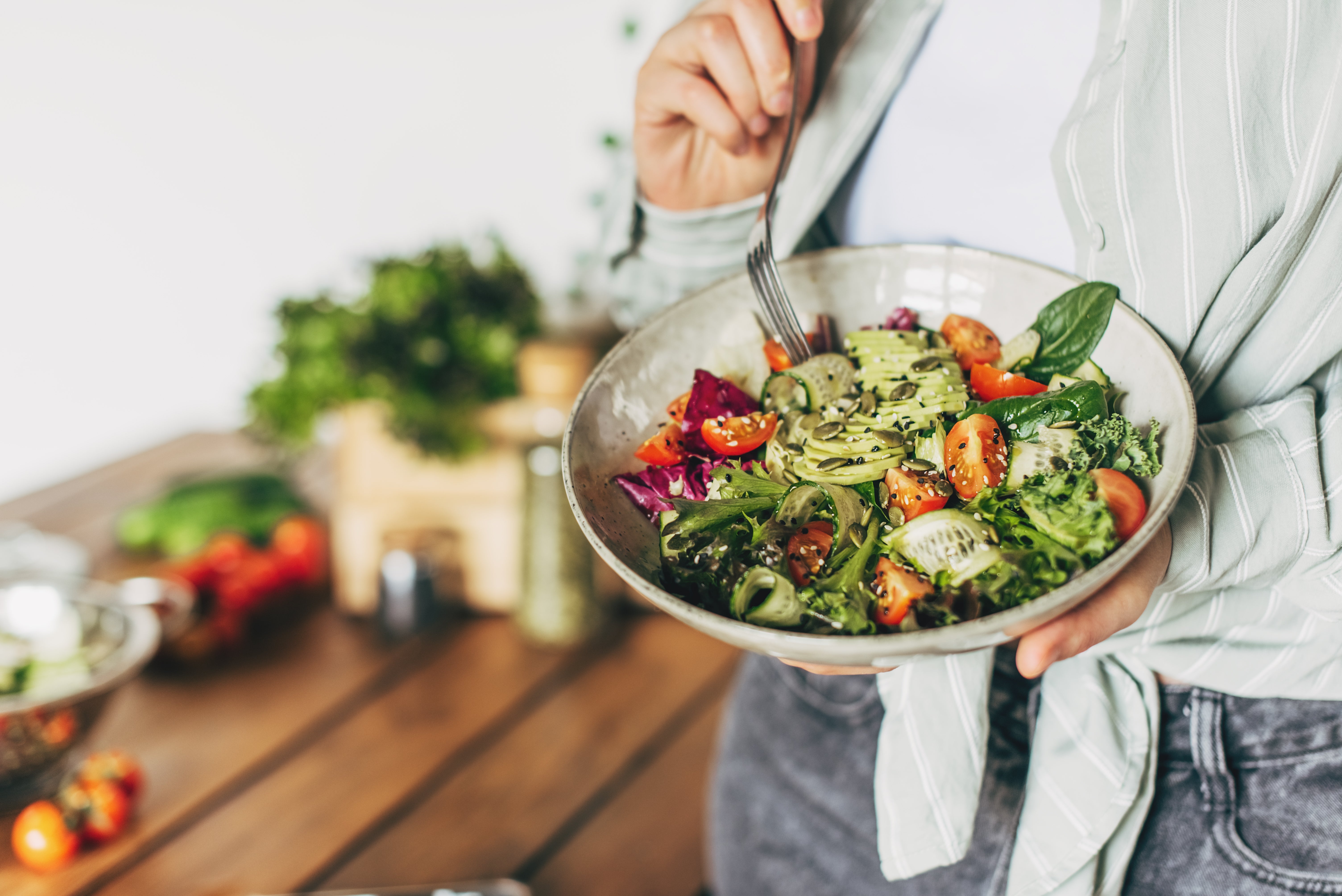 Person holding a vessel of caller crockery with greens, cherry tomatoes, and cucumbers successful a room setting