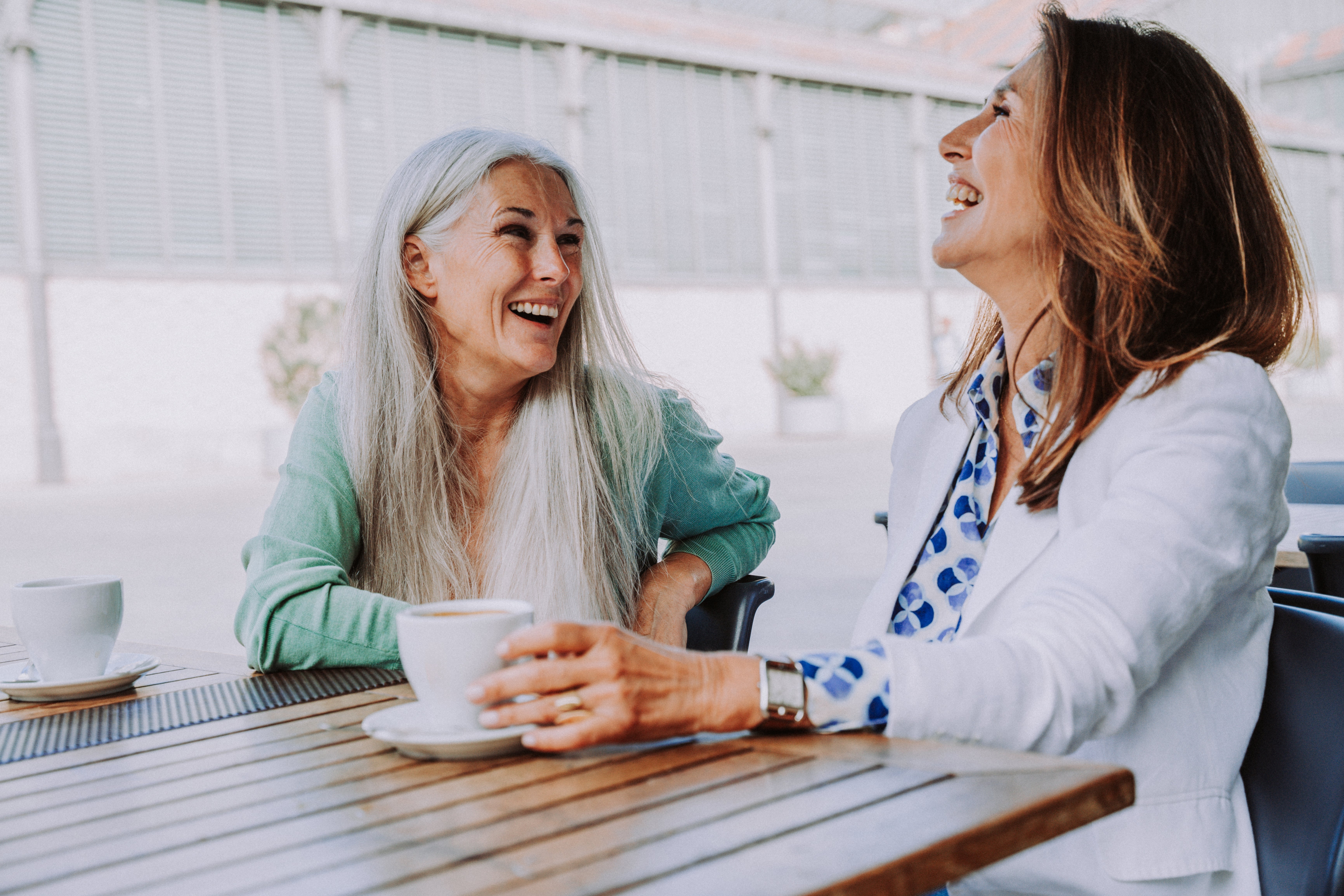 Two women sitting astatine an outdoor café, laughing and enjoying java together