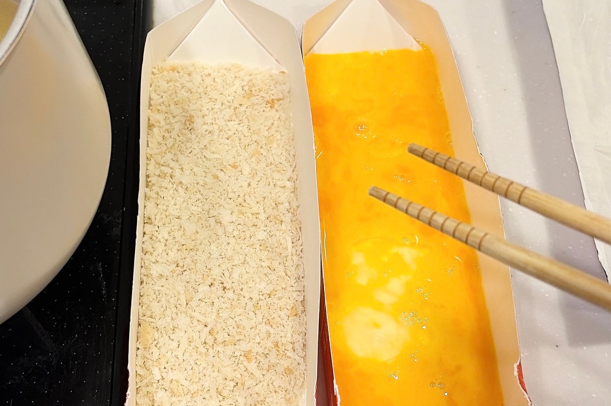 パン粉と卵液が入った紙パックのトレイに箸が添えられたシーン。料理の準備中。