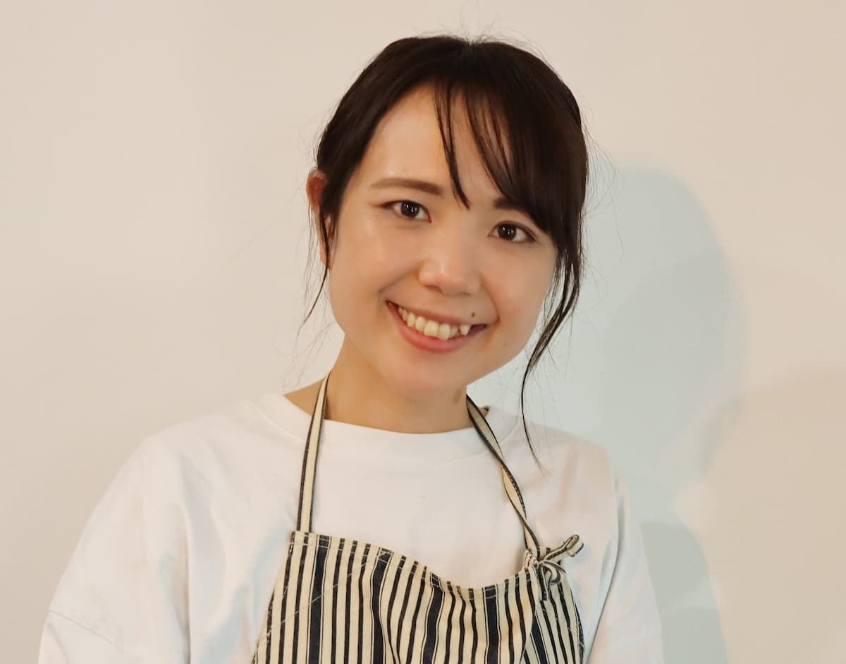 エプロンを着た女性が微笑んでカメラを見つめています。