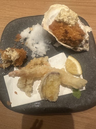 牡蠣フライ、塩、フリッター、おろし生姜、レモンのくし形切りが黒い皿に盛られている。