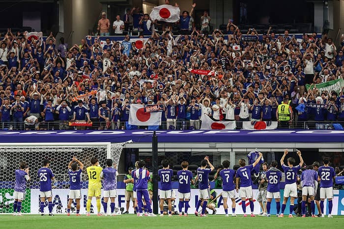Soccer squad  stands facing cheering fans holding flags successful  a stadium; post-match appreciation moment